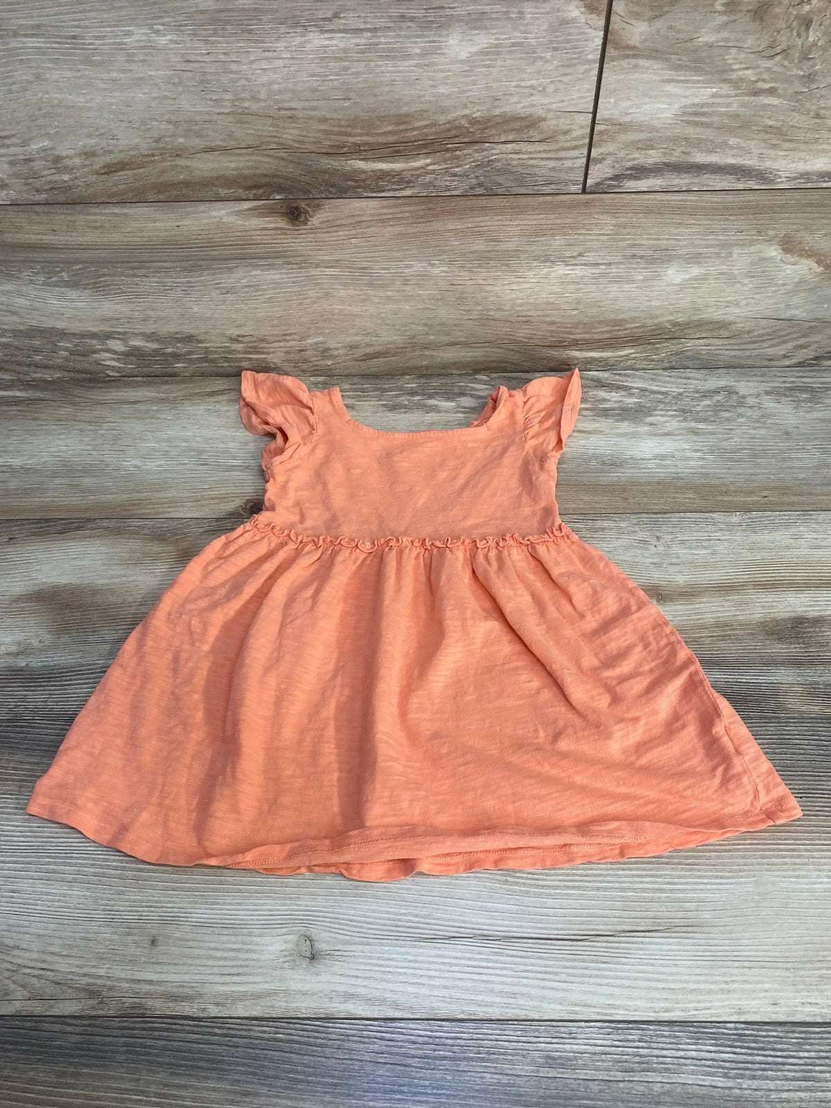 Flat lay of Cat and Jack peach baby dress, size 18 months, with flutter sleeves and gathered waist on wood background