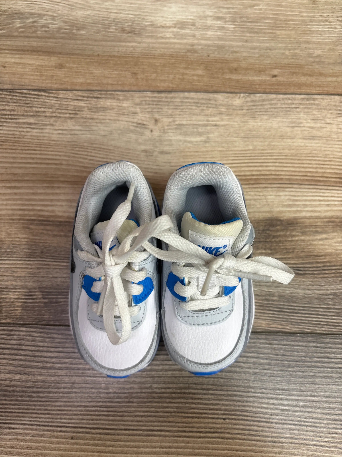 Top view of Nike Air Max 90 Leather TD White Photo Blue sneakers showcasing white leather uppers with blue accents on wood