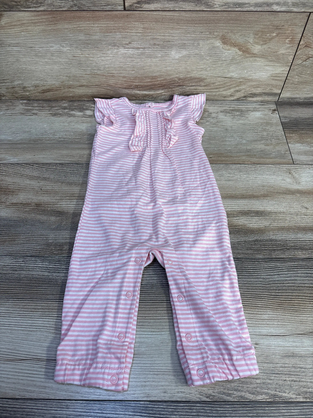 Front view of the Simple Joys pink striped ruffle jumpsuit showcasing ruffle neckline and legs with a wood-grain background