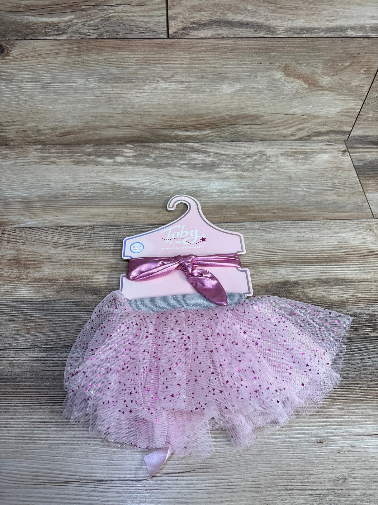 Pink baby tutu skirt with sparkly stars, 0-12 months, displayed on a wood background