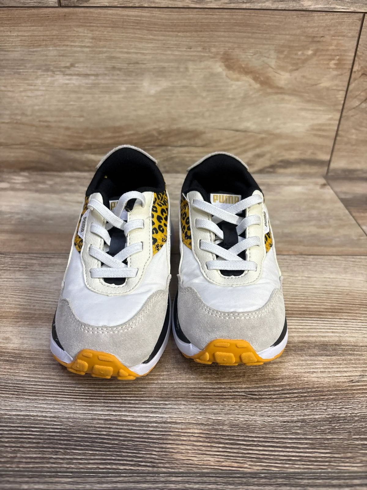 Front view of Puma Seeker Leo low-top sneakers with leopard side panels, white suede toes and yellow soles on wood background