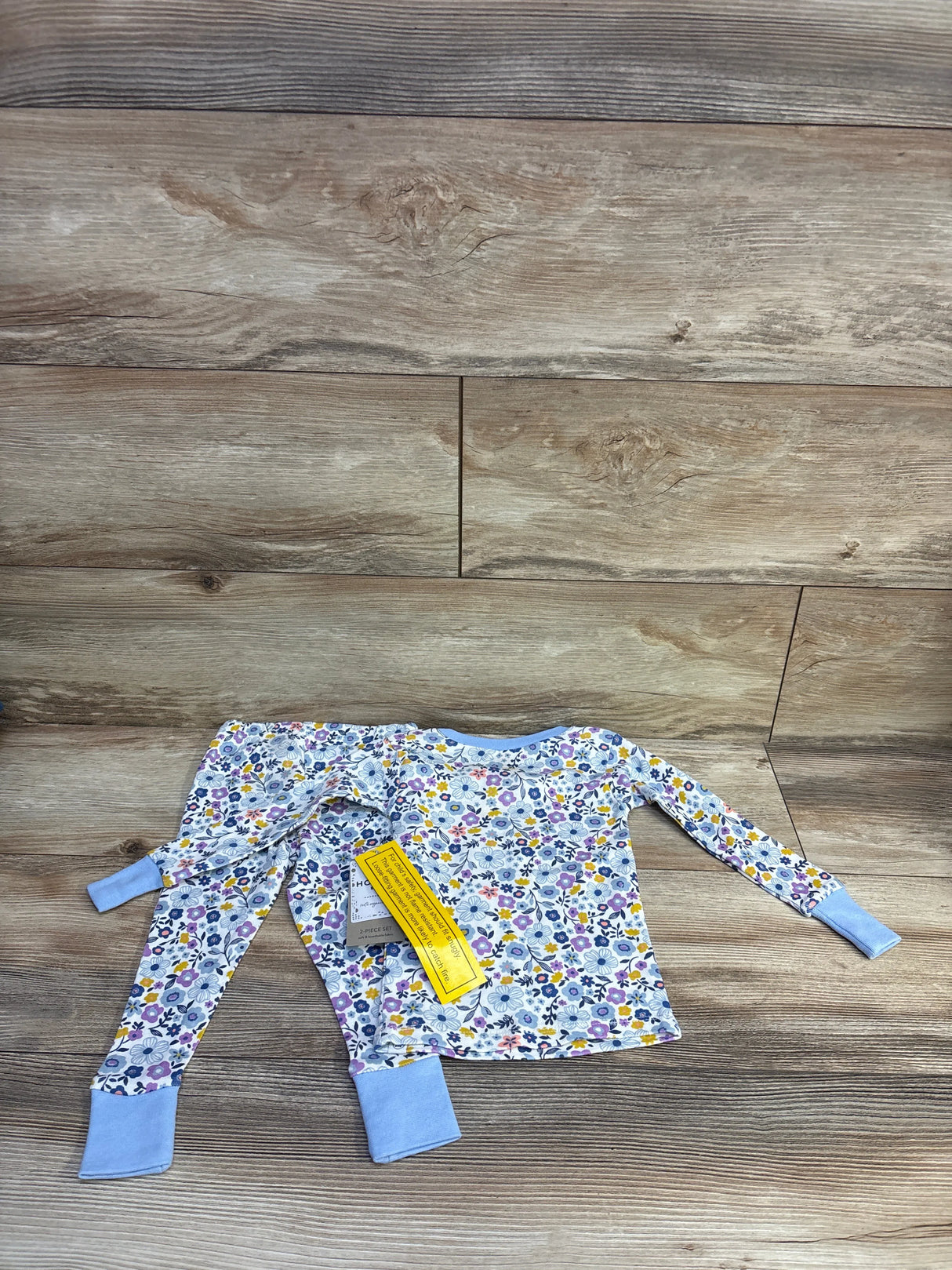 Flat lay of 2-piece Honest Baby organic toddler pajama set showing white floral print and blue cuffs on wood background