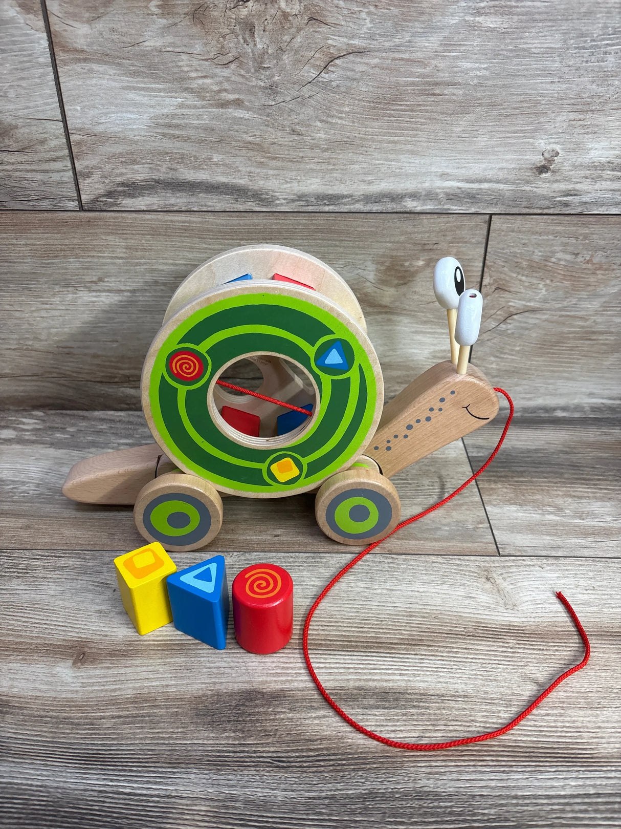 Wooden pull-along snail toy with colorful geometric blocks on wood floor