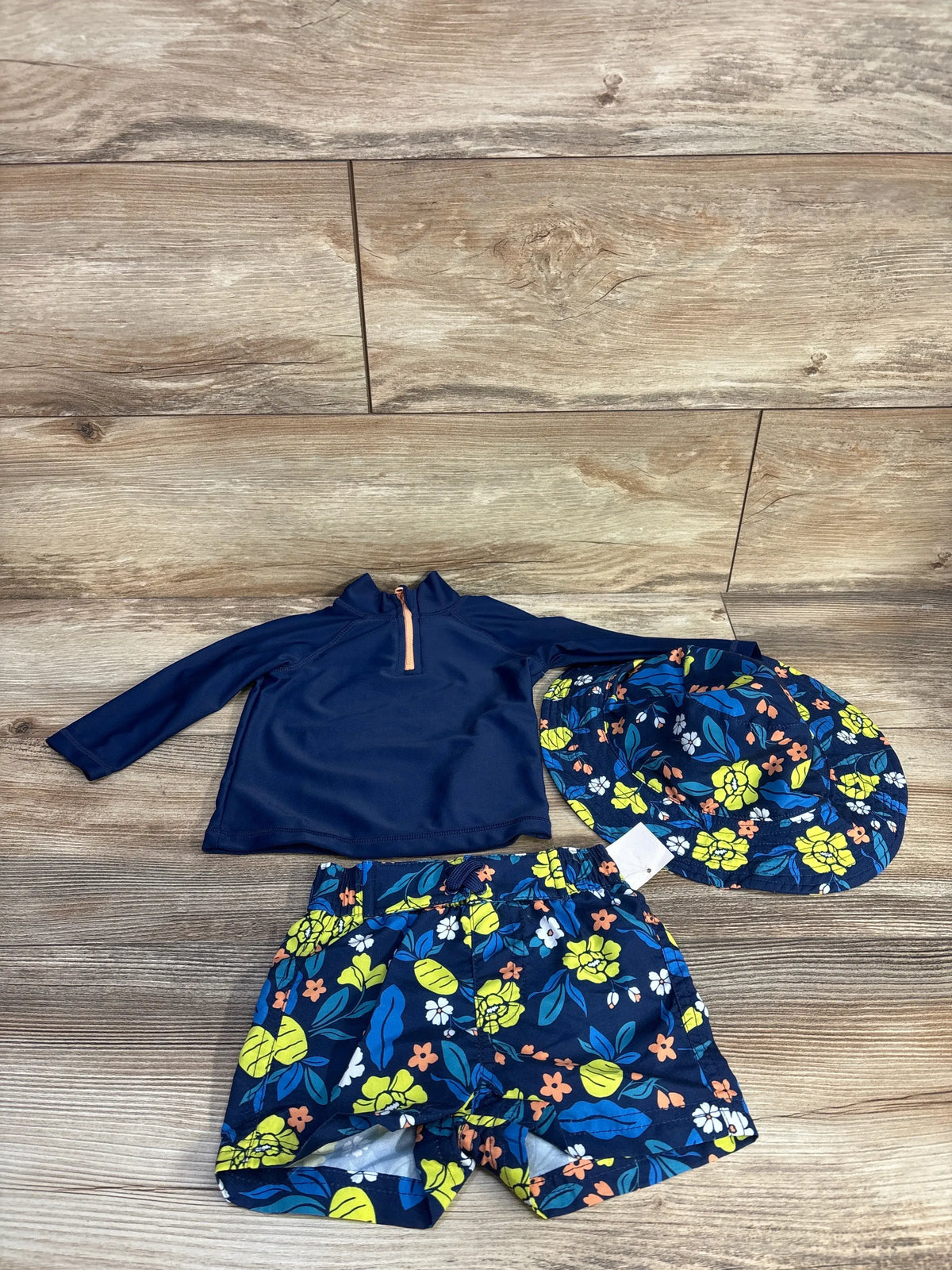 Overhead view of First Impression three piece swim set showing navy rash guard, floral trunks, and matching hat