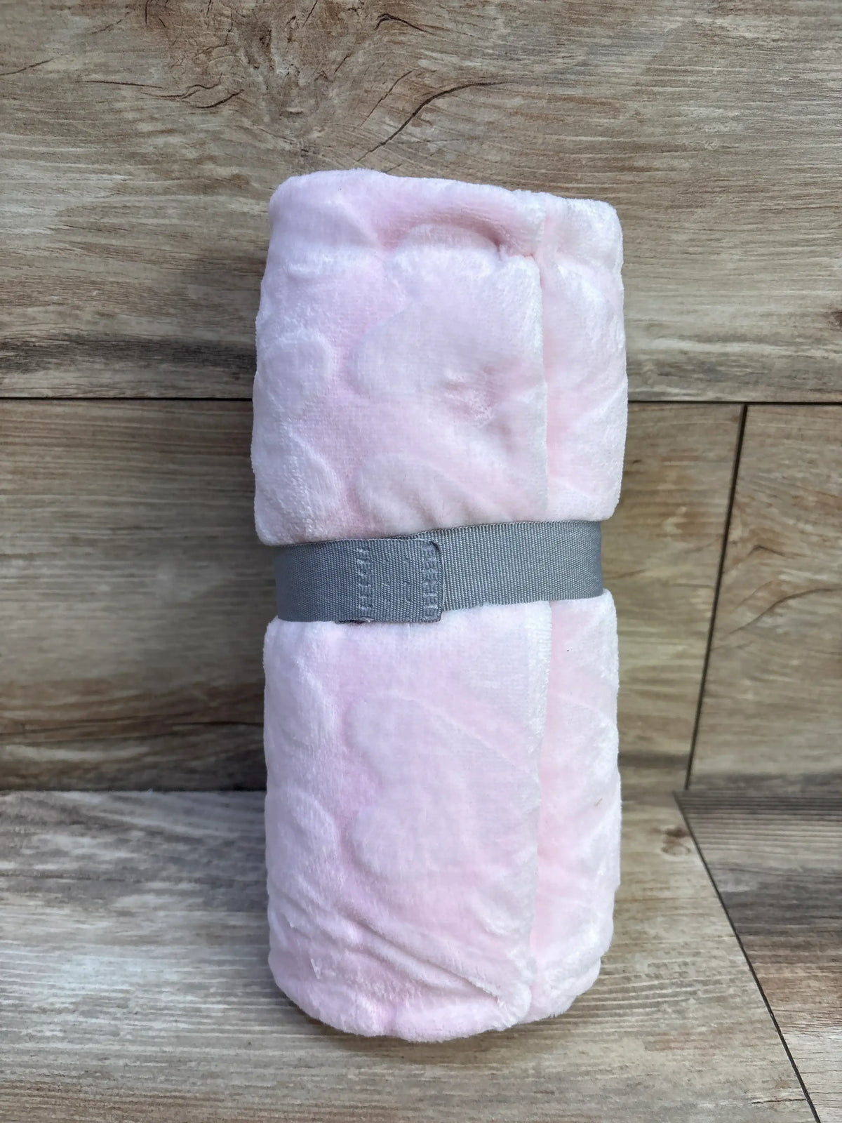 Rolled view of Cloud Island hearts embossed baby blanket in pink showing heart texture on wood background