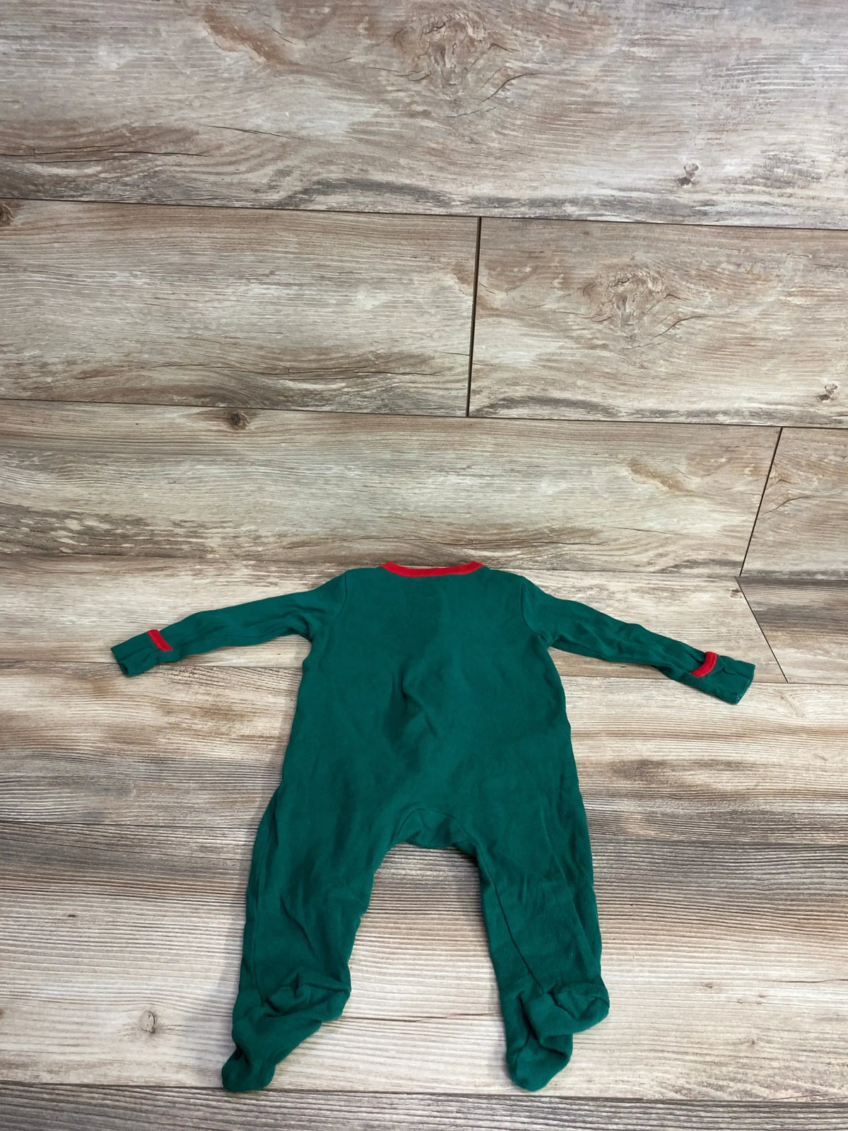 Green baby footed pajamas with red trim, laid flat on wood floor