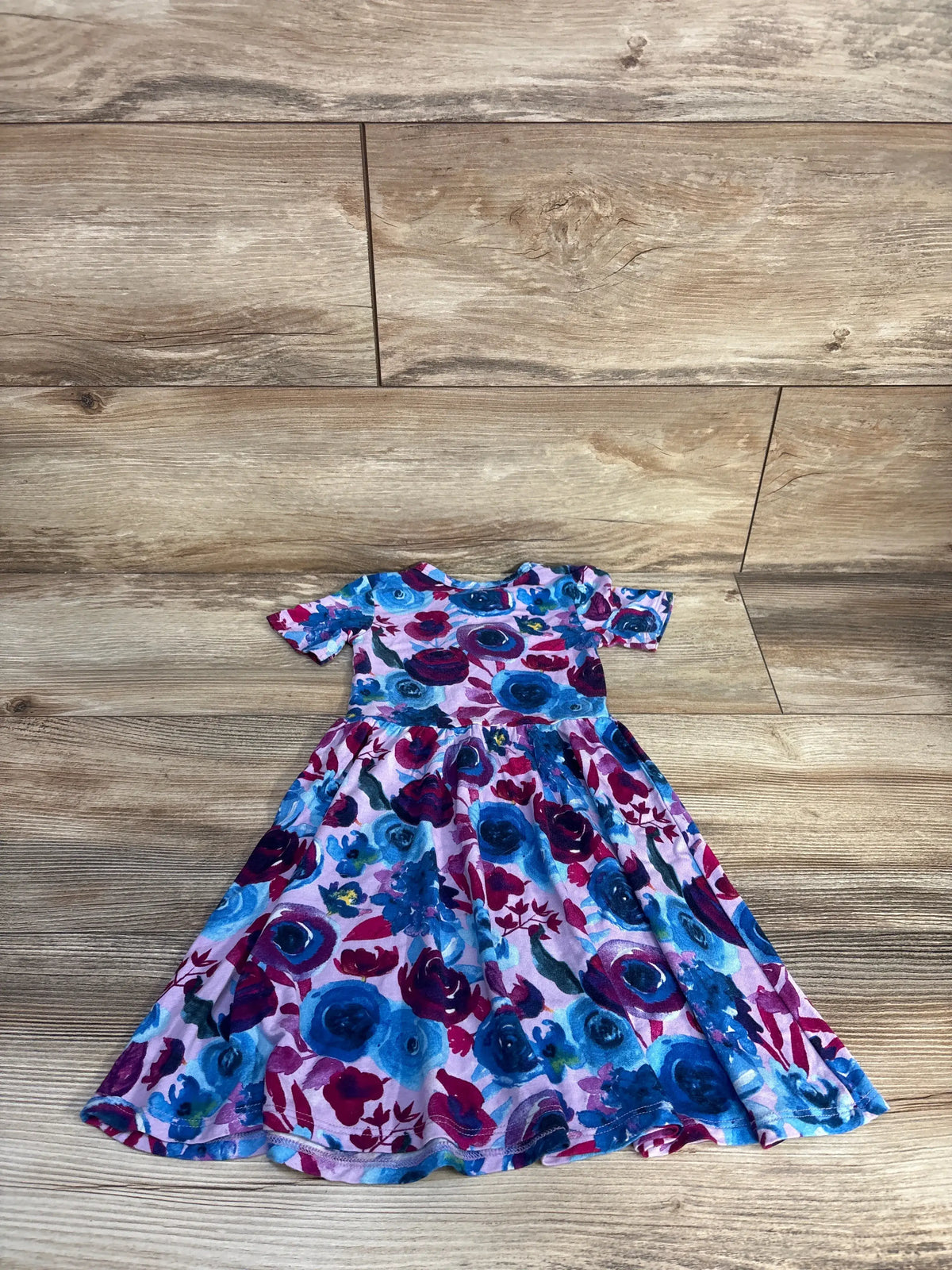 Front view of Gigi & Max floral bamboo tutu dress in purple showcasing colorful floral print and twirly skirt on a wood floor