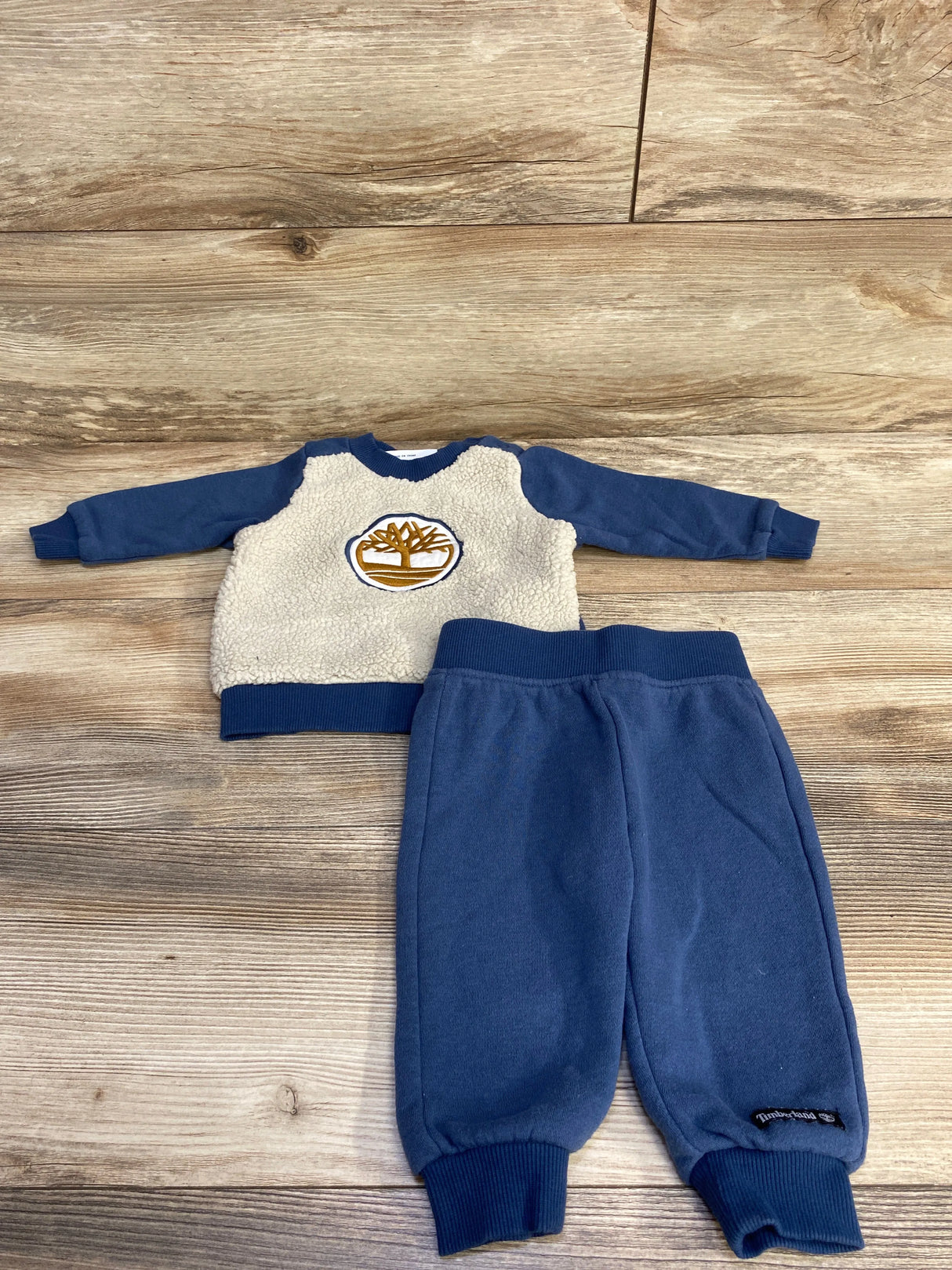 Kids blue fleece Timberland sweater with white sherpa front and matching blue sweatpants on wood floor