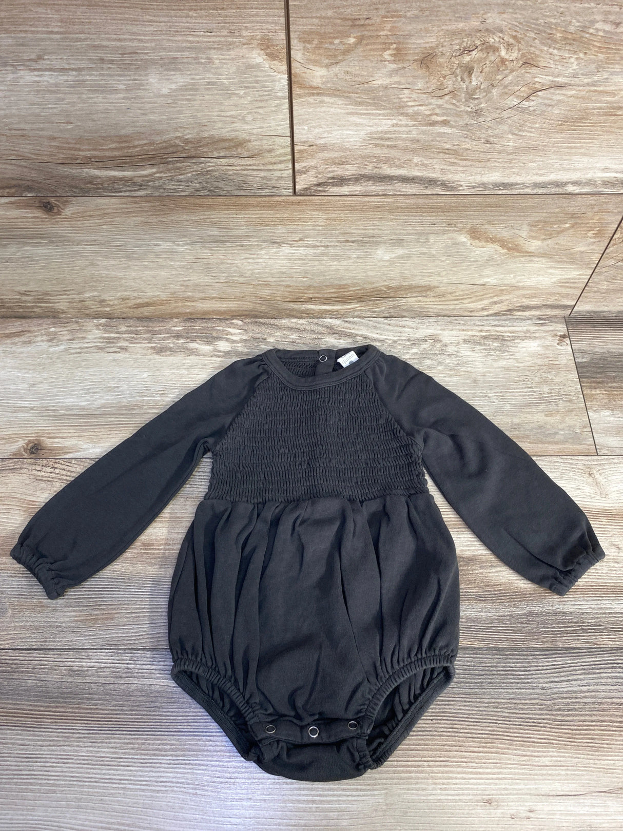 Black long sleeve baby romper with smocked chest and snap buttons on wooden floor