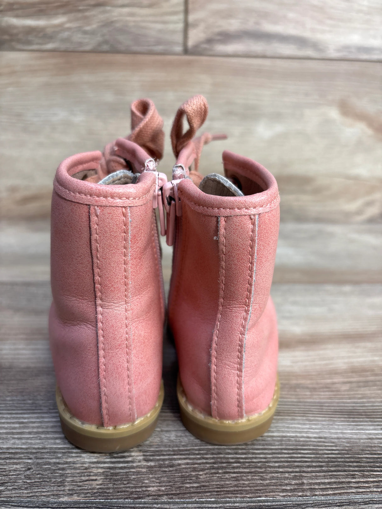 Back view of pink suede toddler boots with beige soles on wooden floor