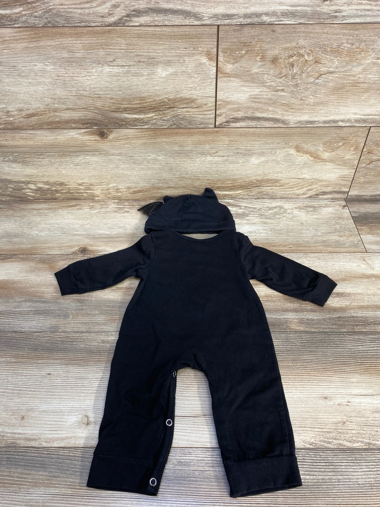 Black baby onesie with hood and ears, laid flat on wood floor
