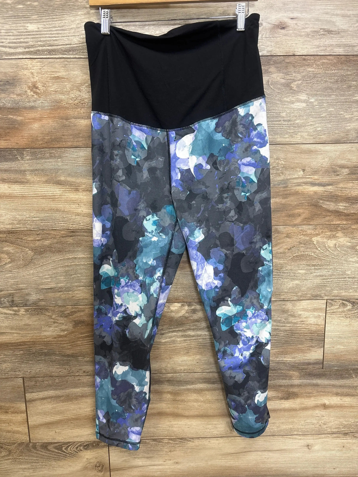 Front view of maternity leggings with black foldover belly panel and blue-purple watercolor floral print on a wooden floor