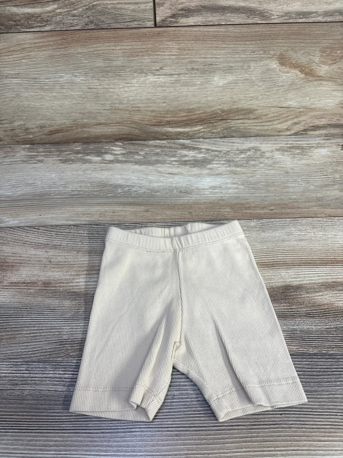 Flat lay of cream ribbed toddler shorts (18 to 24 months) showcasing elastic waistband and knee-length fit on wood background