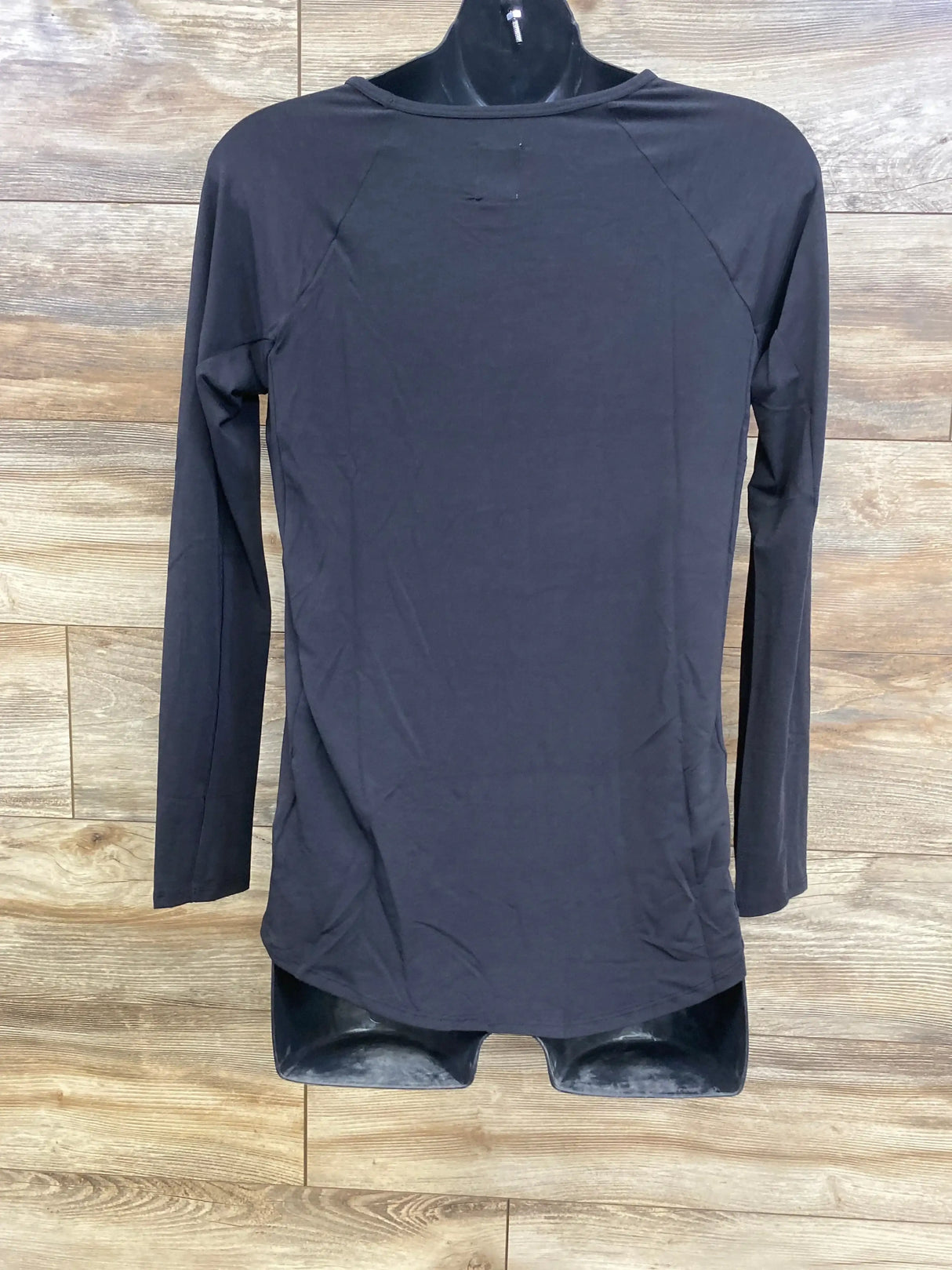 Back view of black Gap maternity long-sleeve shirt (XS) showing raglan sleeves and curved hem on wood plank background