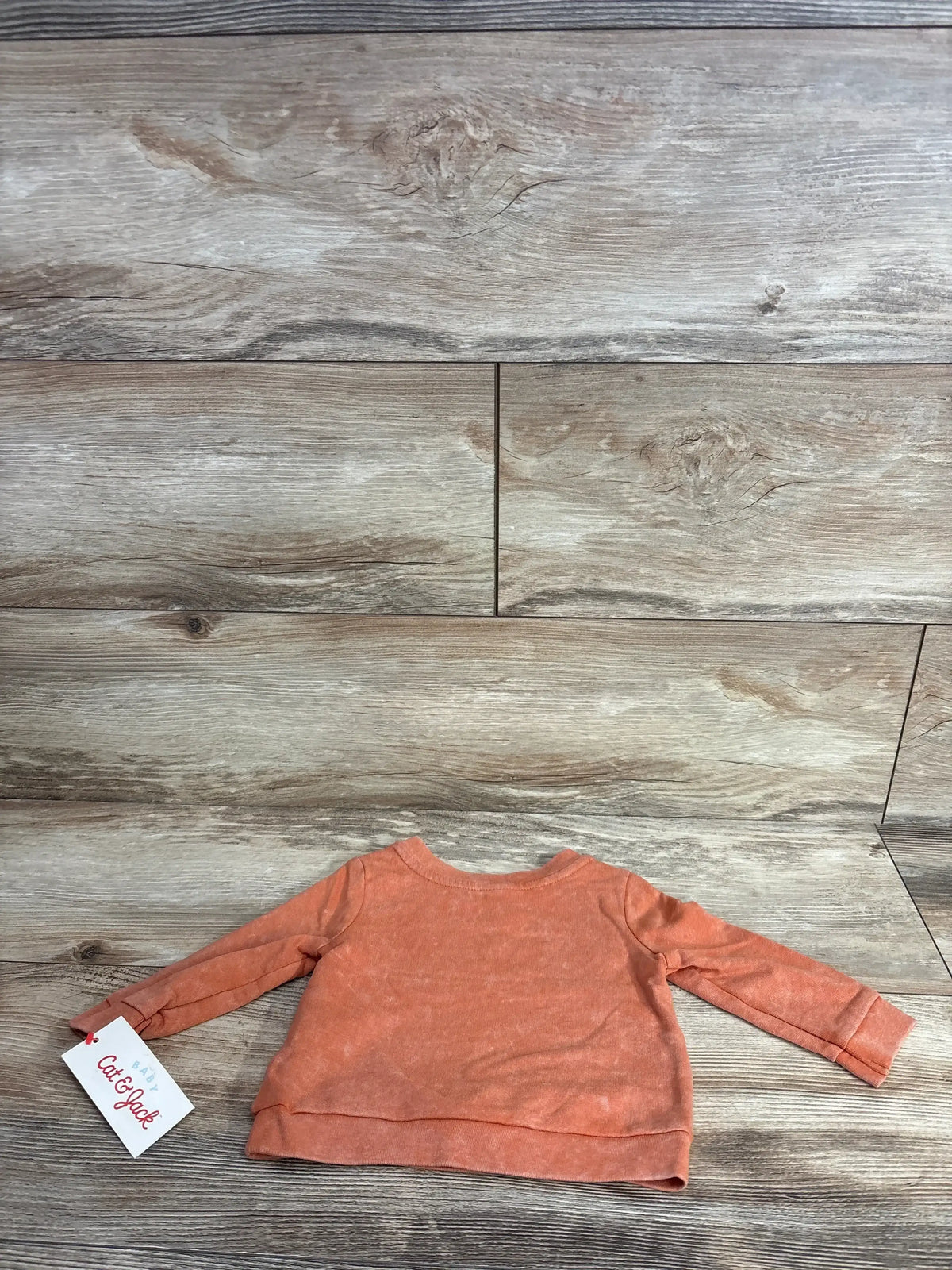 Coral long sleeve baby shirt with tag, laid flat on wood background