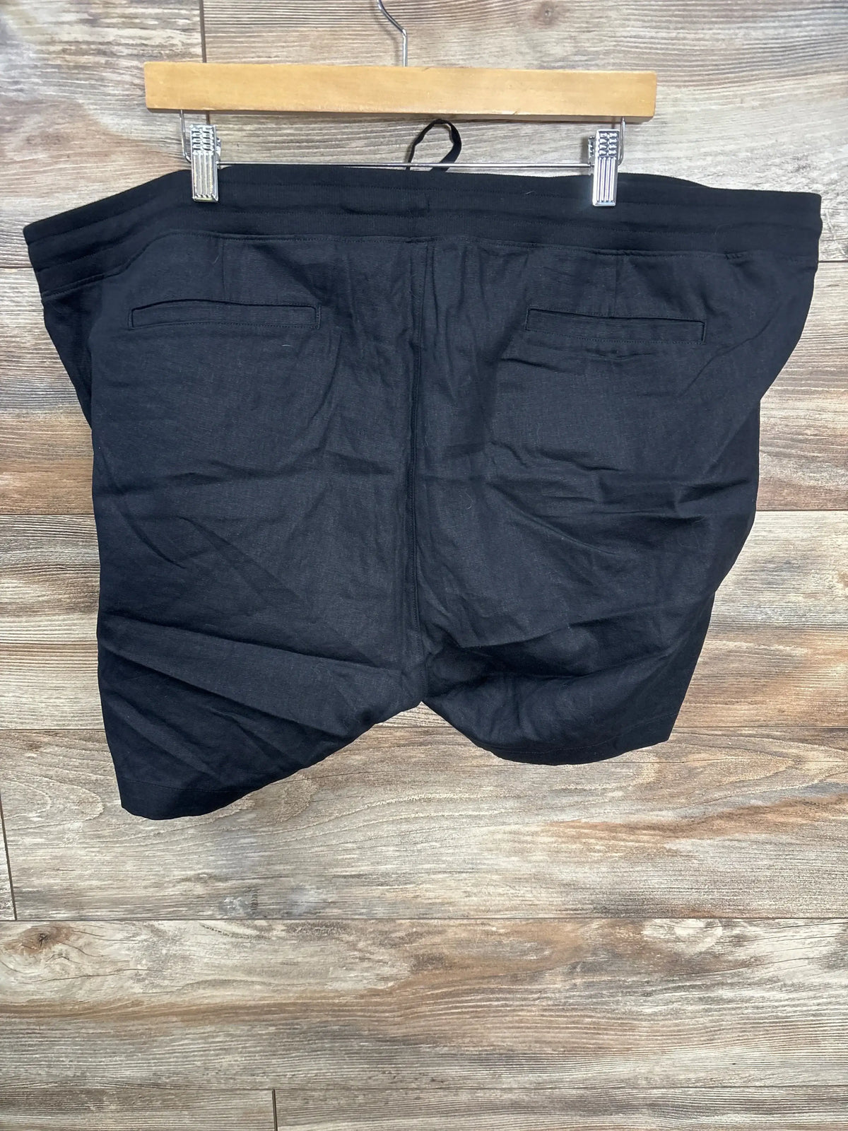 Back view of Gap maternity under-belly black linen-cotton shorts XXL showing two welt back pockets on wooden hanger against wood background