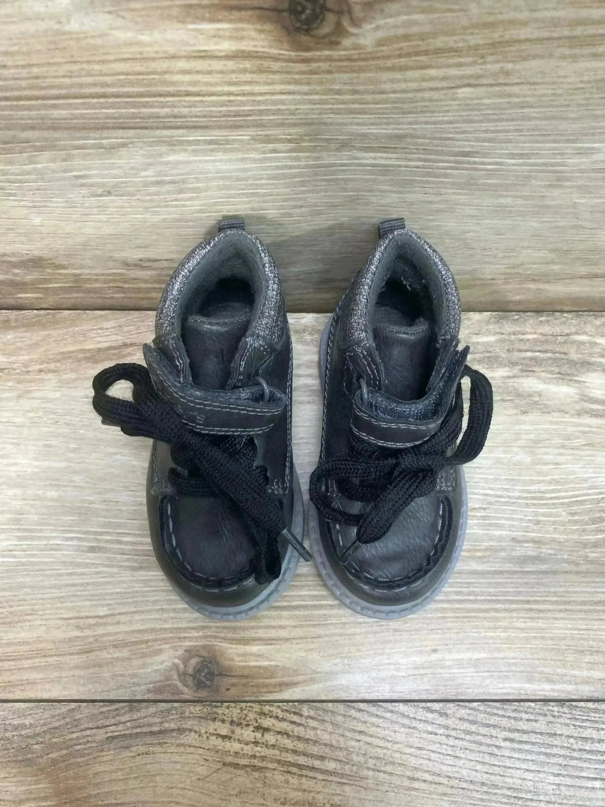Top-down view of Norman toddler ankle boots showing black laces, Velcro strap and stitched details on wood background