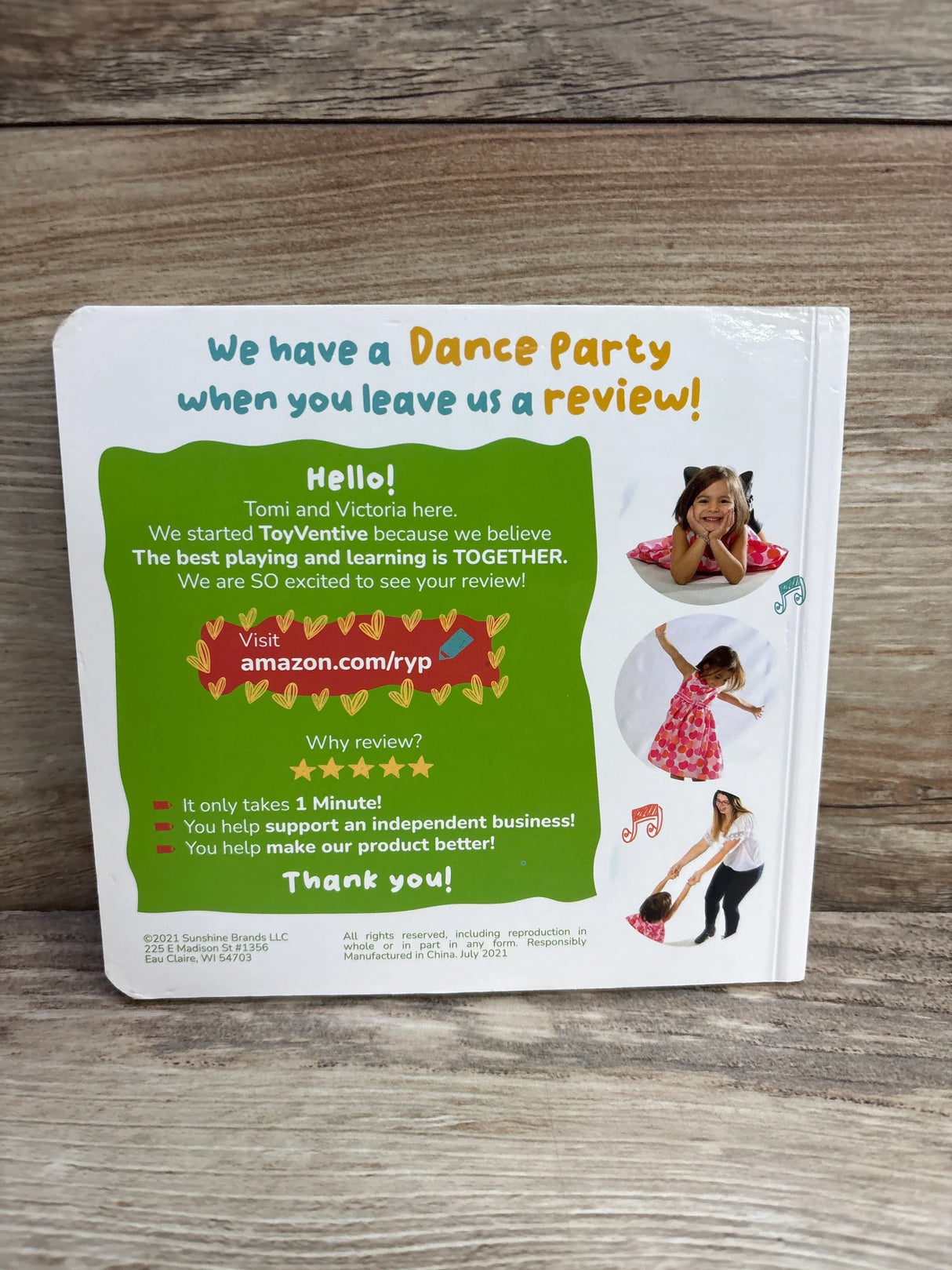Back view of Essential Words board book showing green review request panel and three circular child photos on wood surface