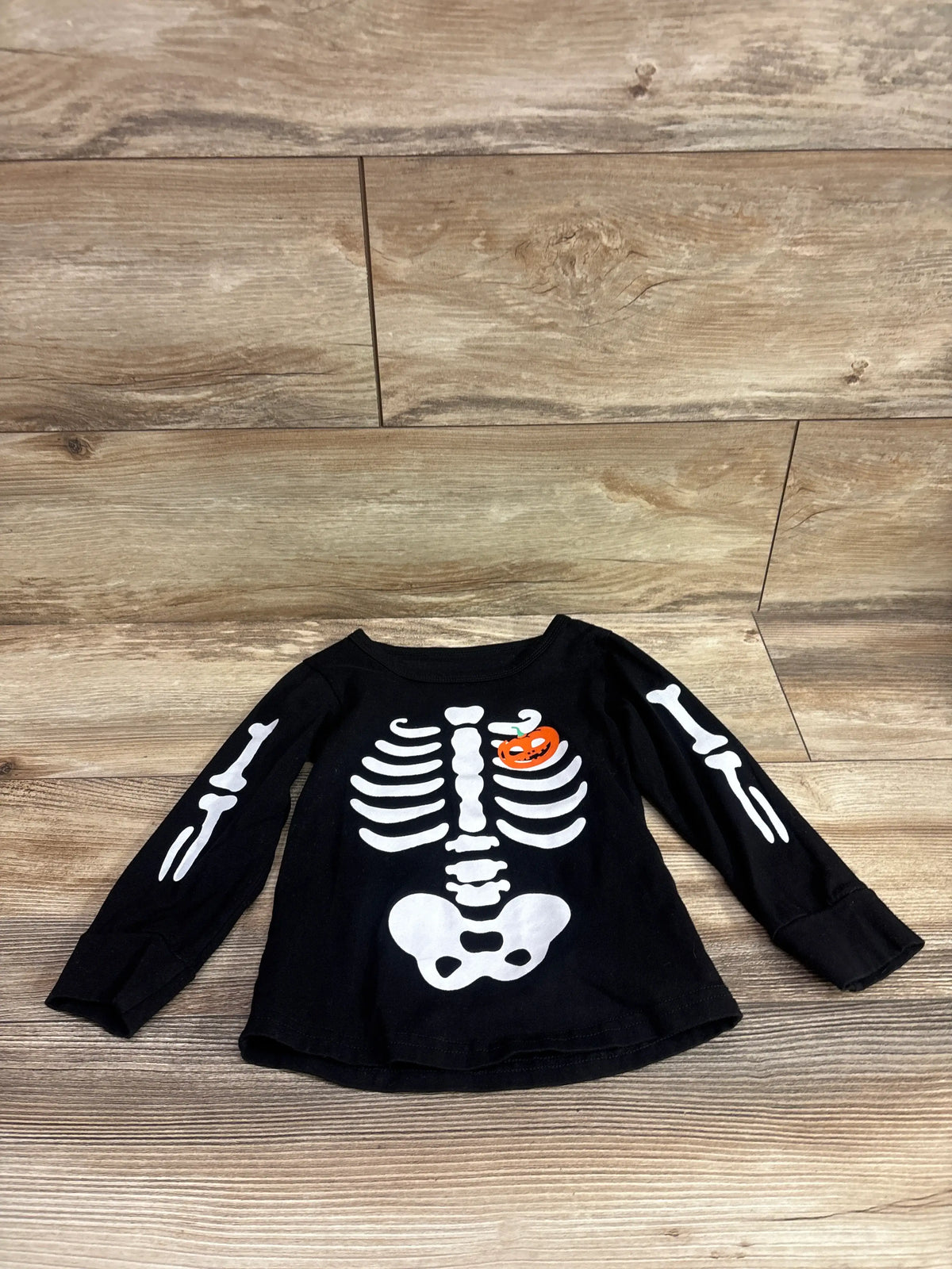 Front view of black GiLiling Halloween skeleton shirt with white skeleton graphics and orange pumpkin detail on wood