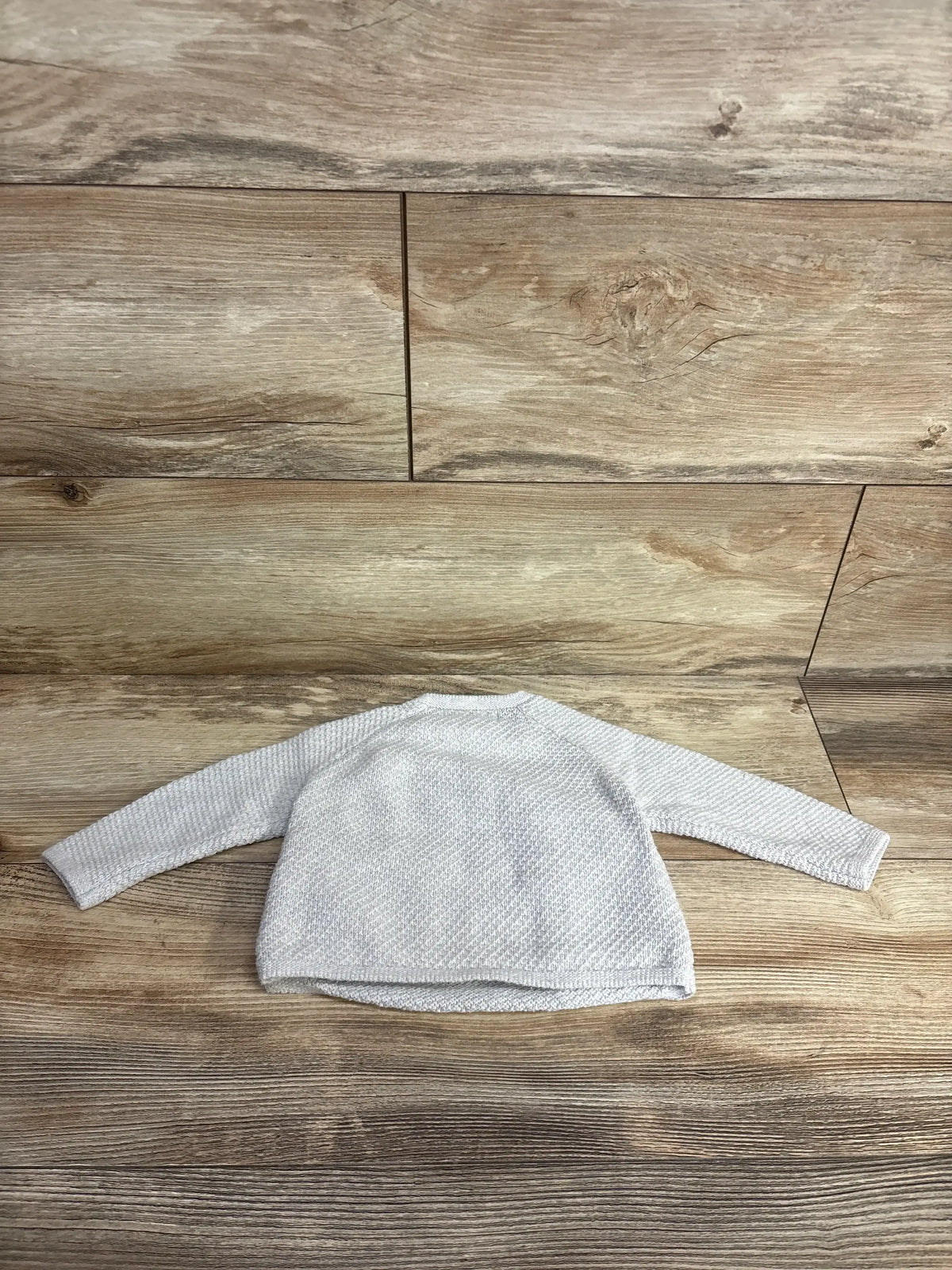 Light gray knit long sleeve baby sweater on wood background