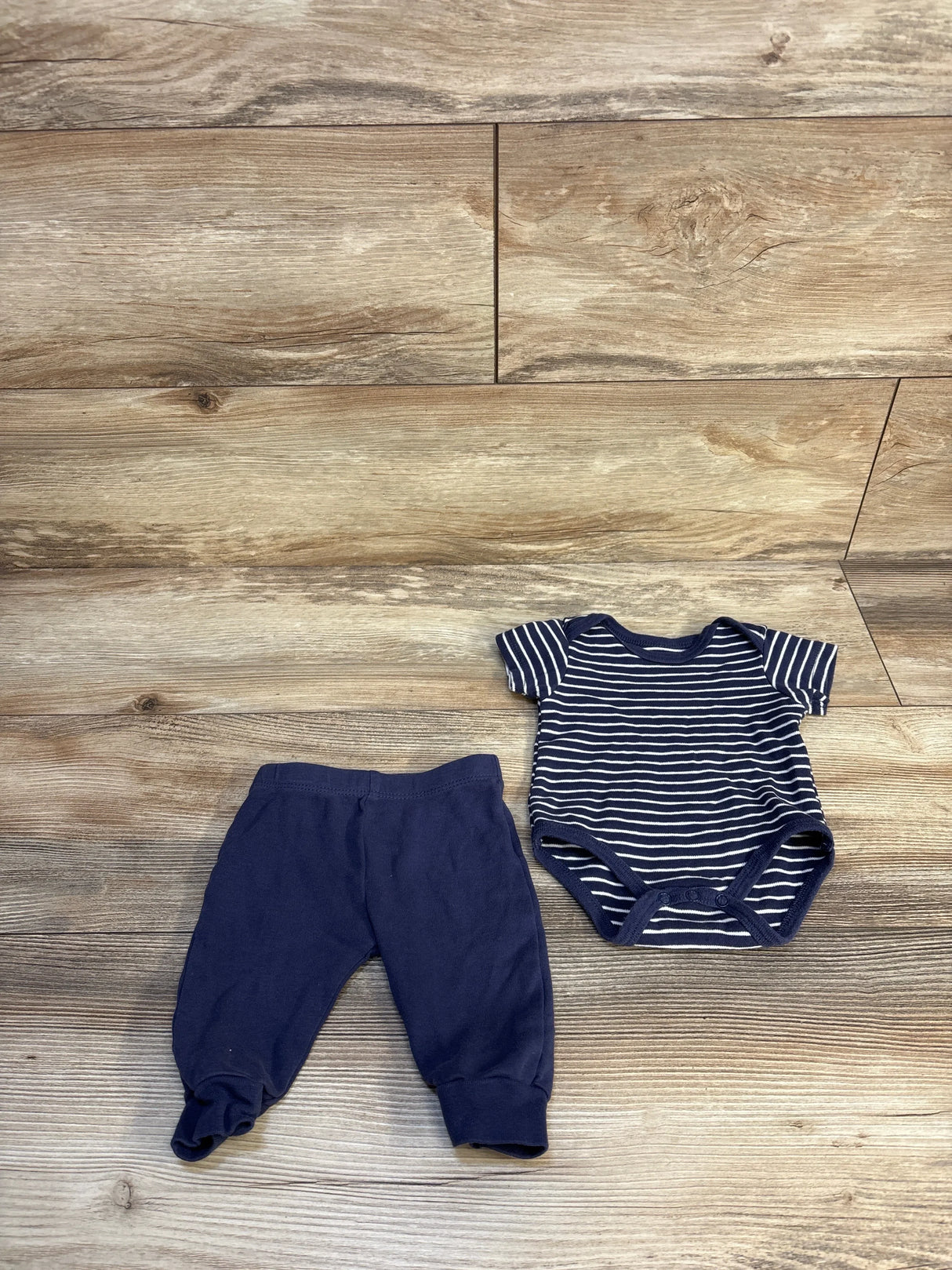 Navy blue baby pants and striped bodysuit set on wood floor, gently used baby clothes