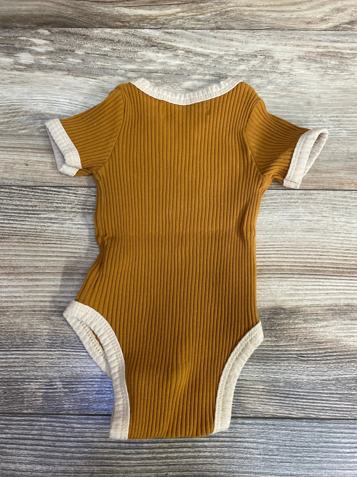 Ribbed short-sleeve mustard yellow baby onesie with cream trim on wooden floor