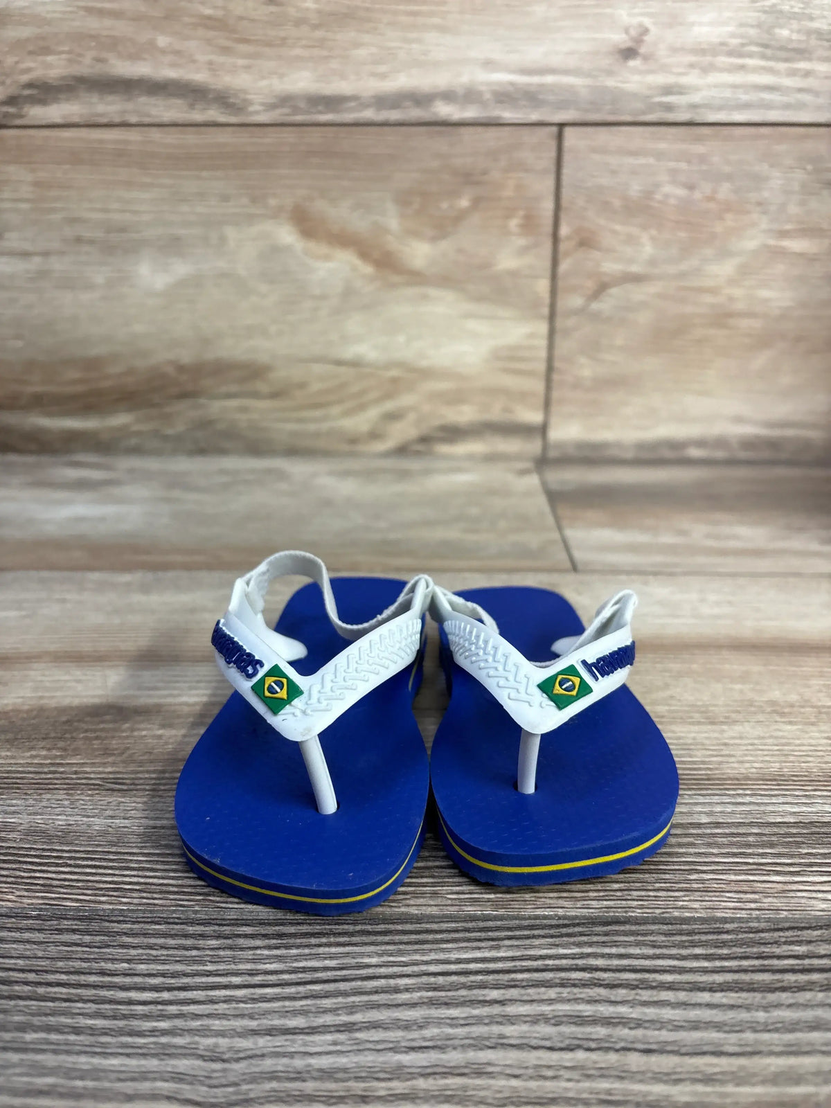 Front view of Havaianas blue flip flops, size 6C, showcasing white elastic ankle straps and thong style on wood-grain floor
