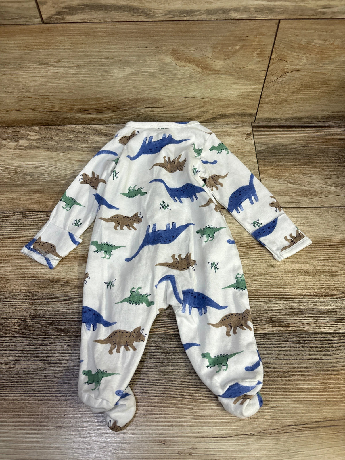 Top view of a white Just One You sleeper in size 3m, showcasing dinosaur prints and footed legs on a wood floor