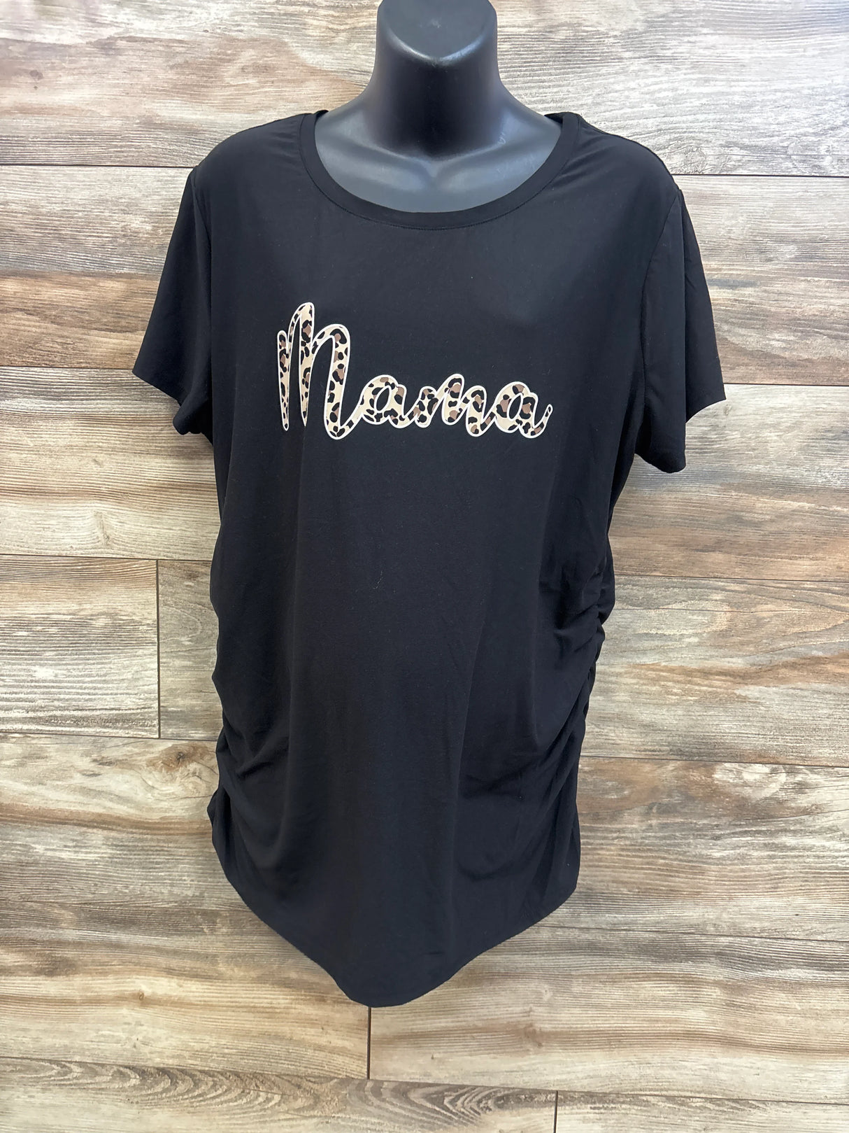Front view of Time and Tru maternity shirt, black with leopard print Mama logo and side ruching on a mannequin with wood background