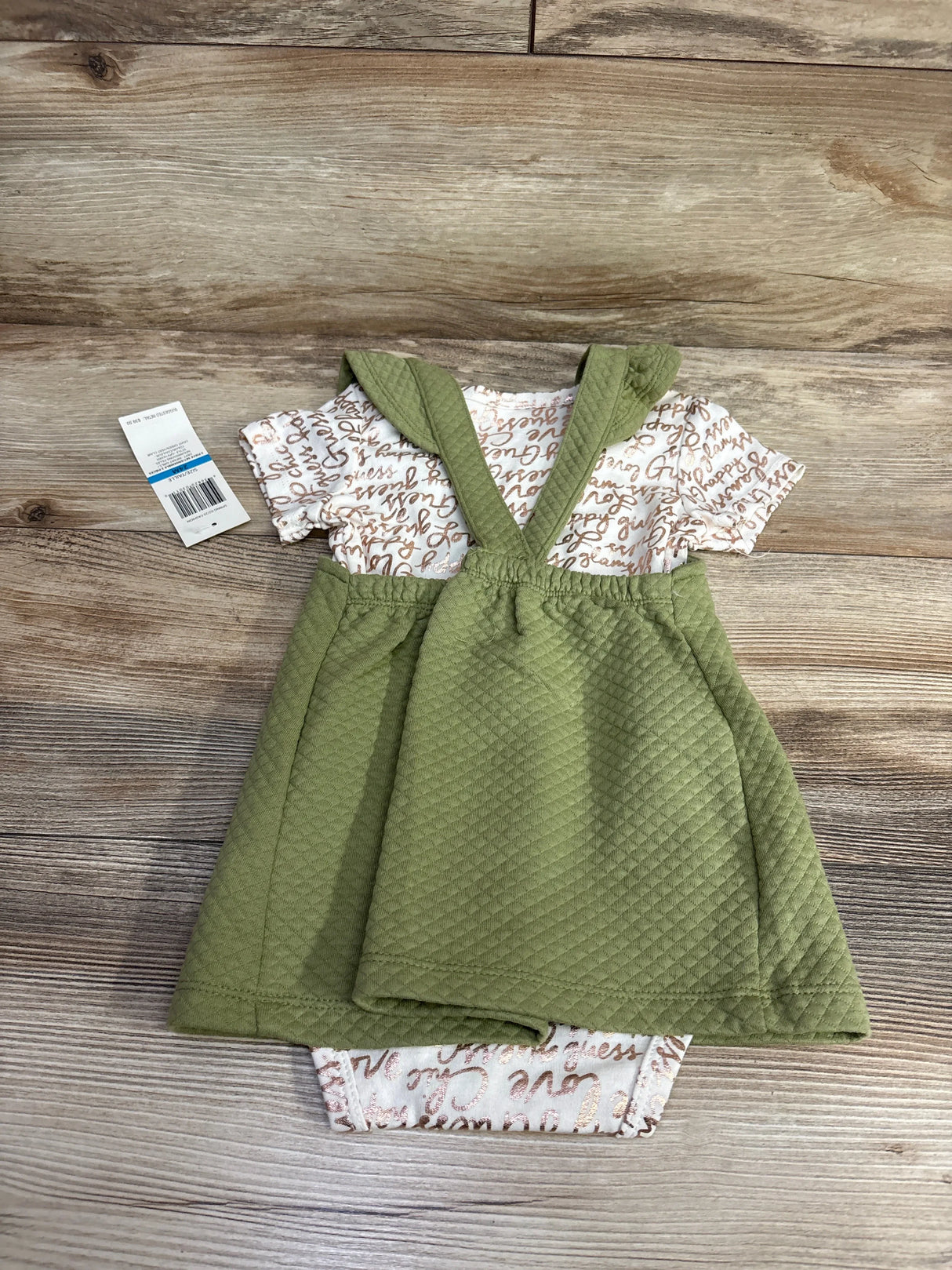 Green baby romper dress with cross-back straps on wood floor, short sleeve printed onesie