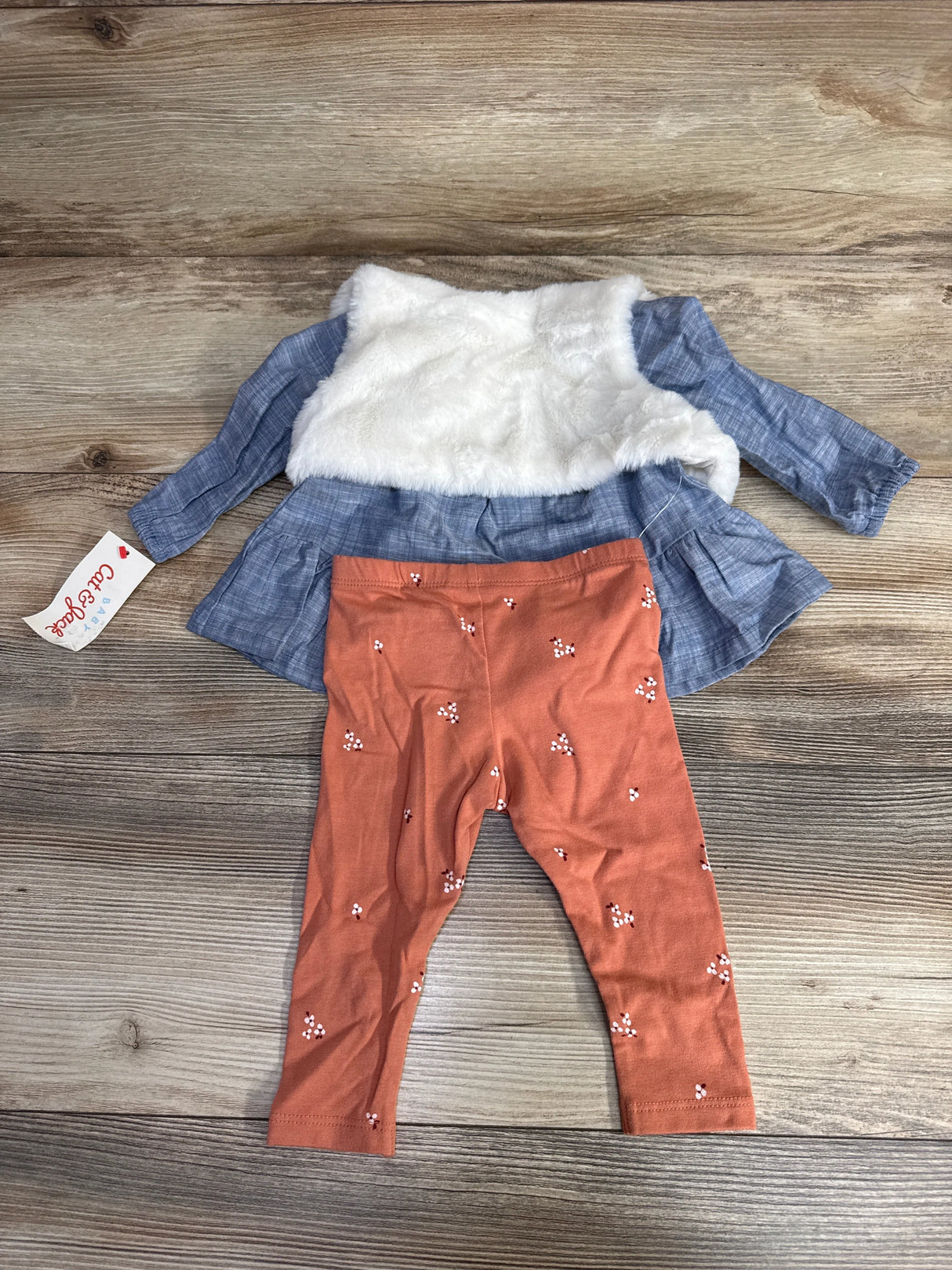 Baby outfit with blue long-sleeve dress featuring white faux fur vest and rust orange floral leggings on wooden floor