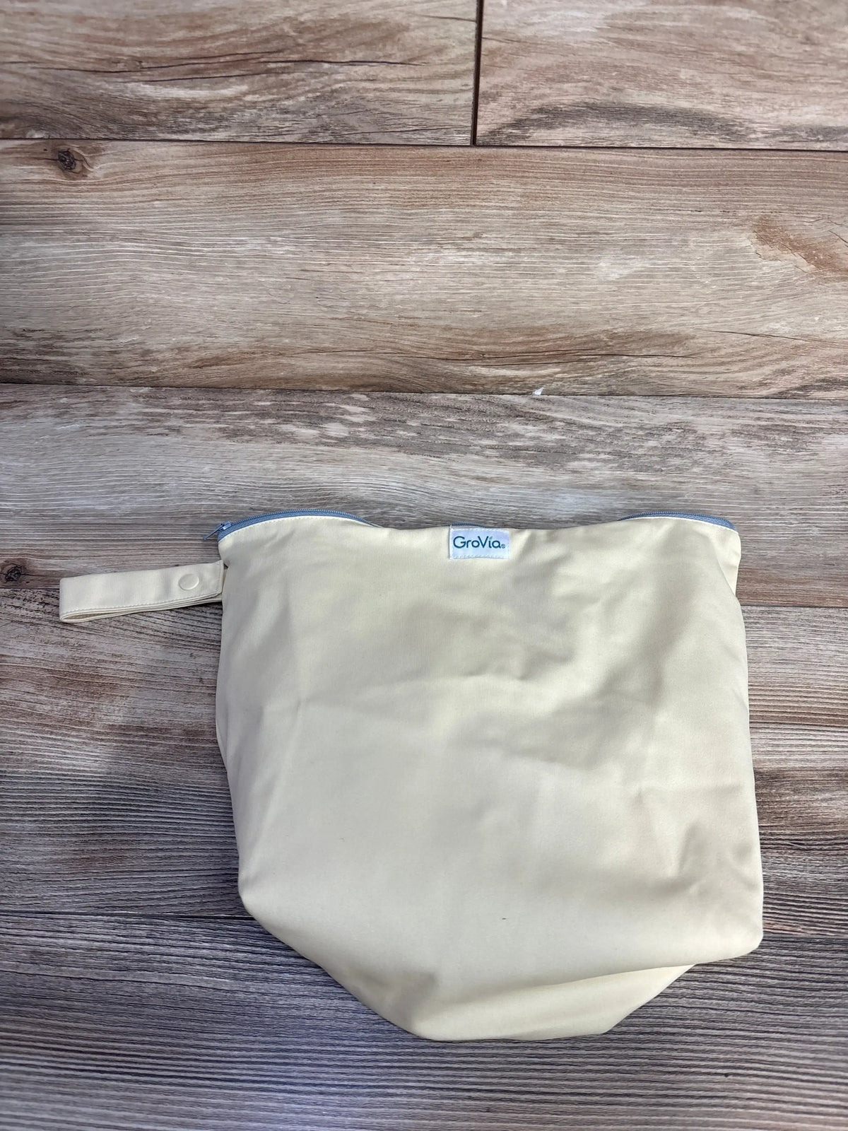 GroVia cream wet bag with strap and zipper on wood floor, reusable diaper storage bag
