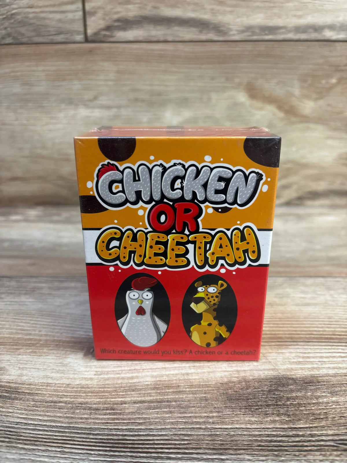 Front view of Chicken or Cheetah card game box showing large CHICKEN OR CHEETAH title and cartoon chicken and cheetah on wooden tabletop background