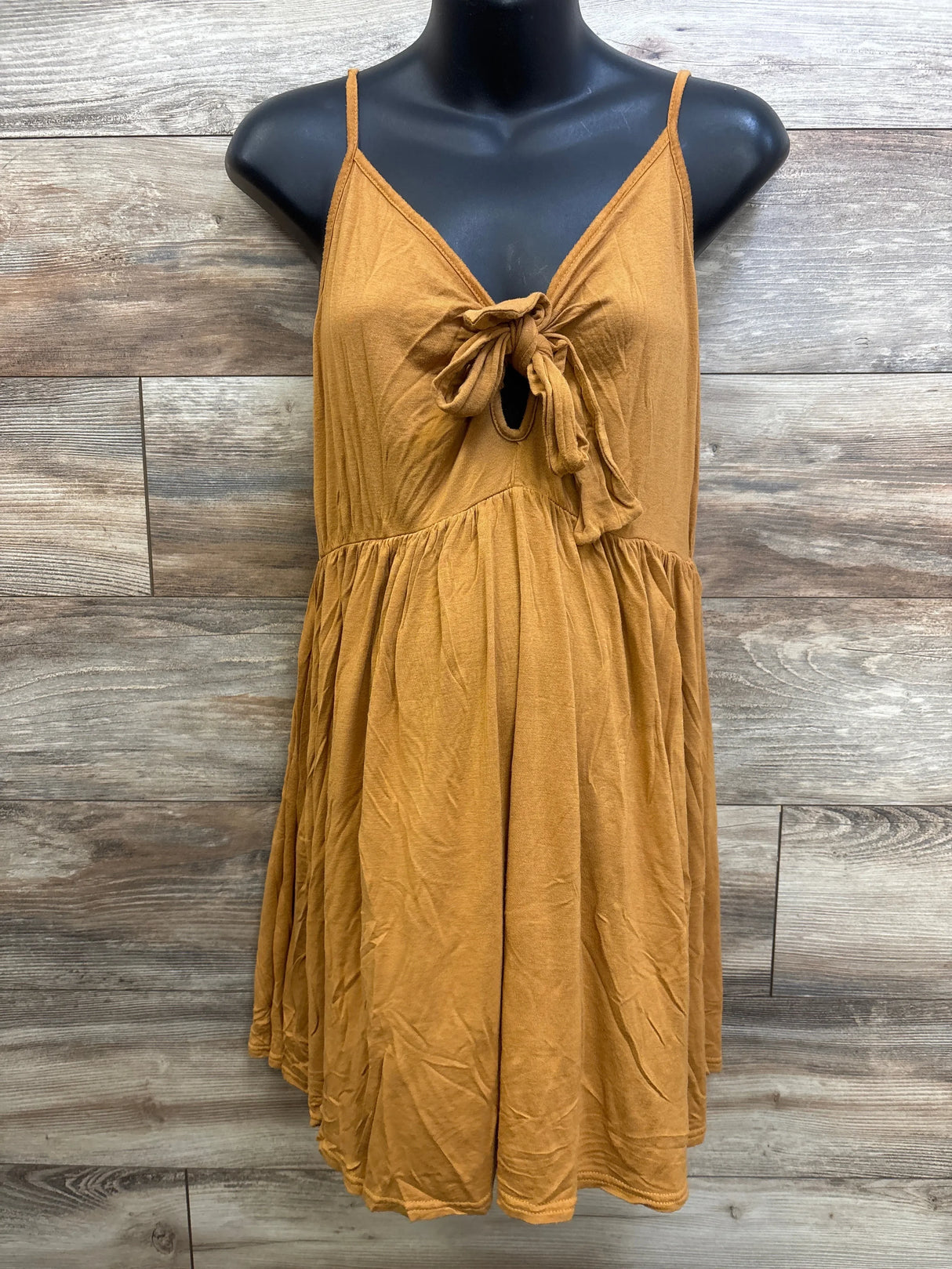 Front view of Boohoo maternity sleeveless dress showcasing front tie knot, empire waist and gathered skirt on mannequin against wood plank background