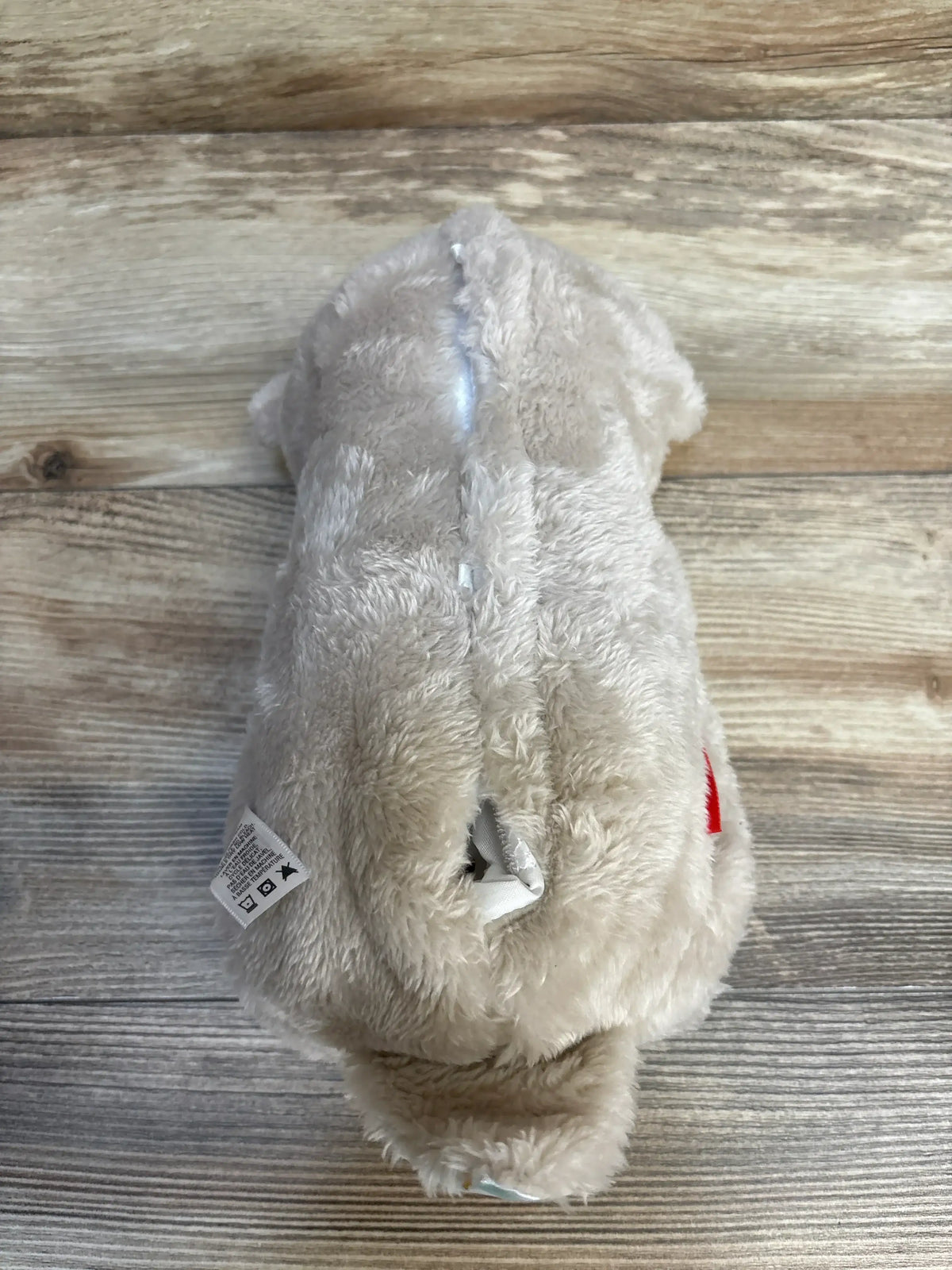 Rear view of Fisher-Price Soothe ‘n Snuggle Otter plush showing beige fur and a small seam opening with care tag on wood background