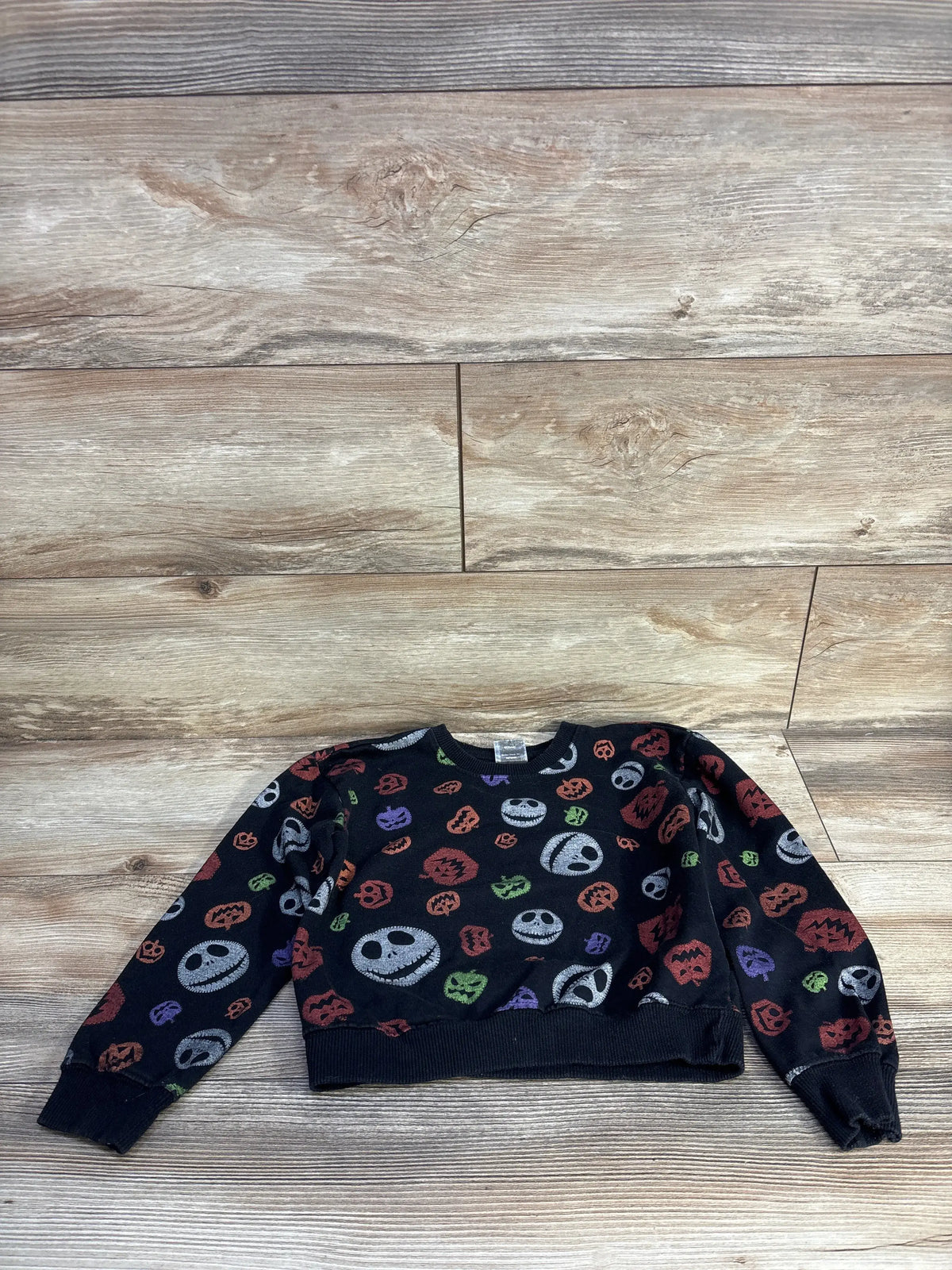Front view of black Disney Nightmare Before Christmas sweatshirt with colorful character and pumpkin prints on a wood floor