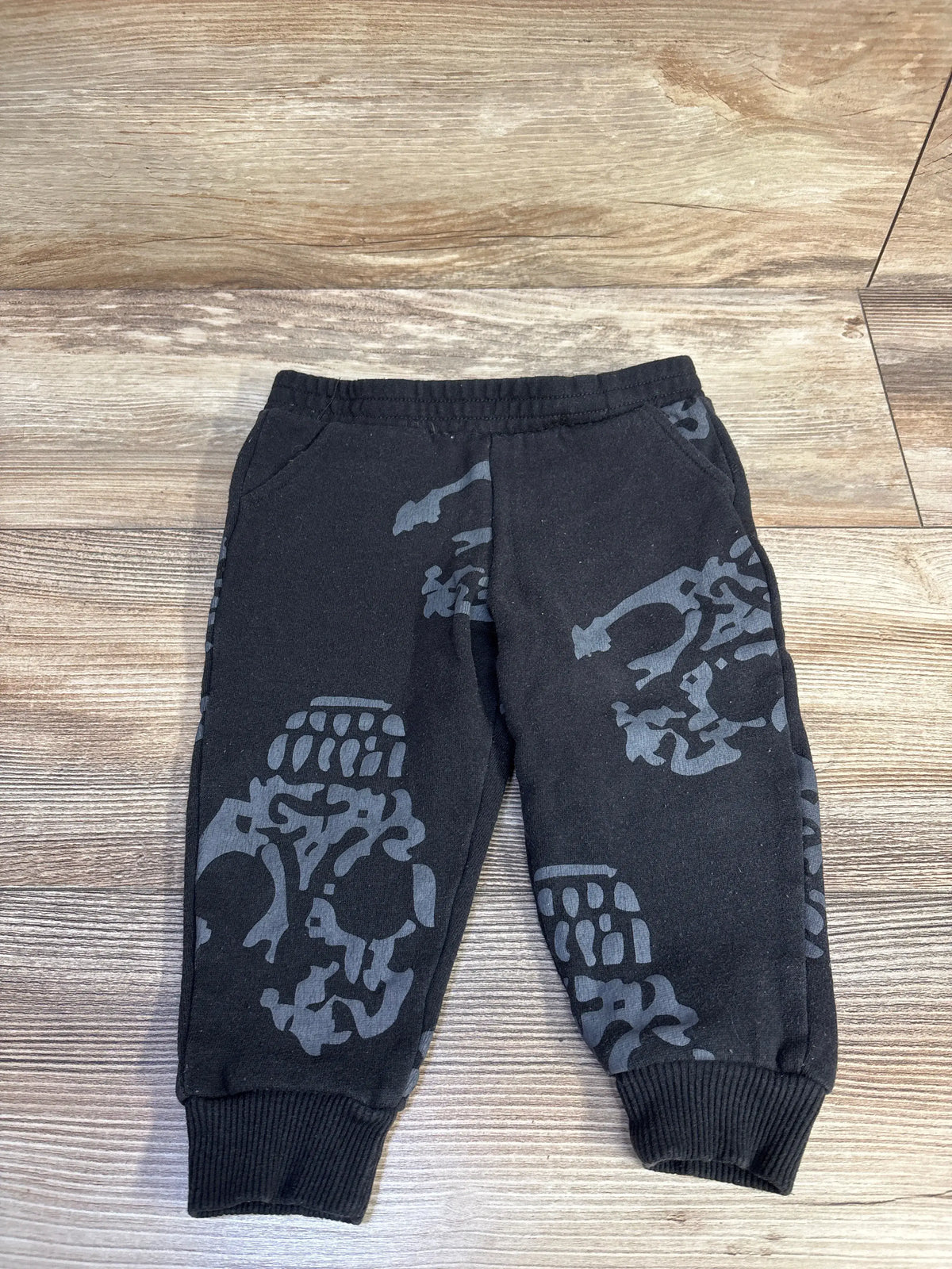 Front view of Beetlejuice black pull-on joggers showcasing gray skeleton graphics and ribbed cuffs on a wood-grain background