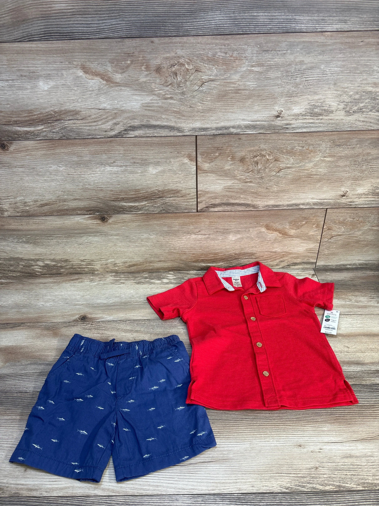 Toddler boy outfit with red button-up shirt and blue shorts with shark print on wood floor