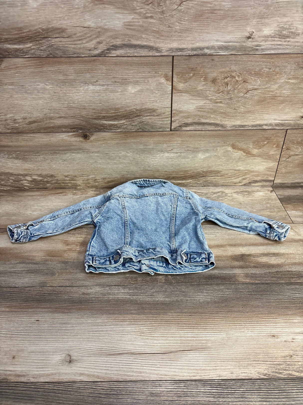 Light blue kids denim jacket displayed flat on a wooden floor background for children's resale