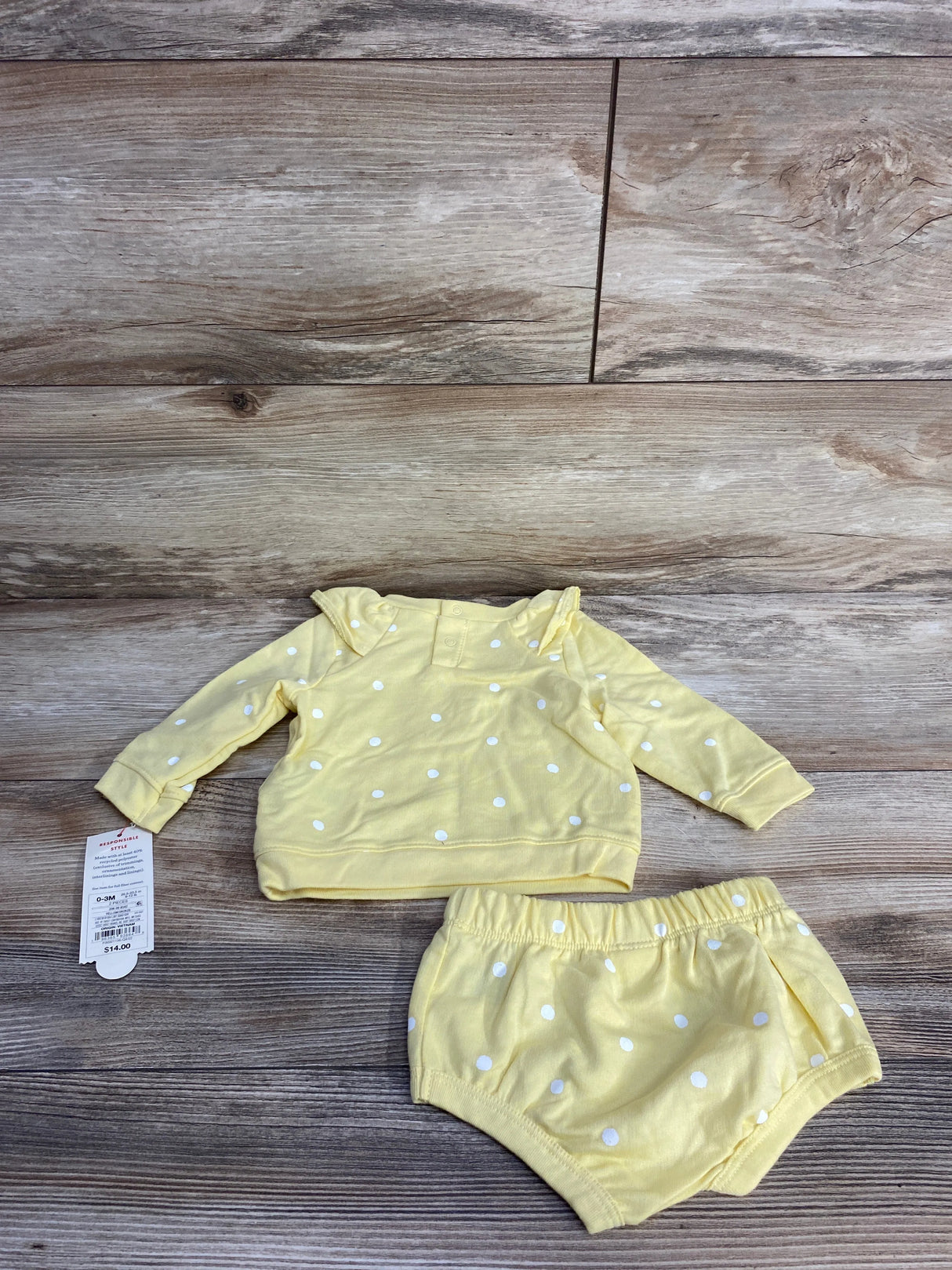 Yellow polka dot baby outfit with long sleeve shirt and matching shorts on wooden background