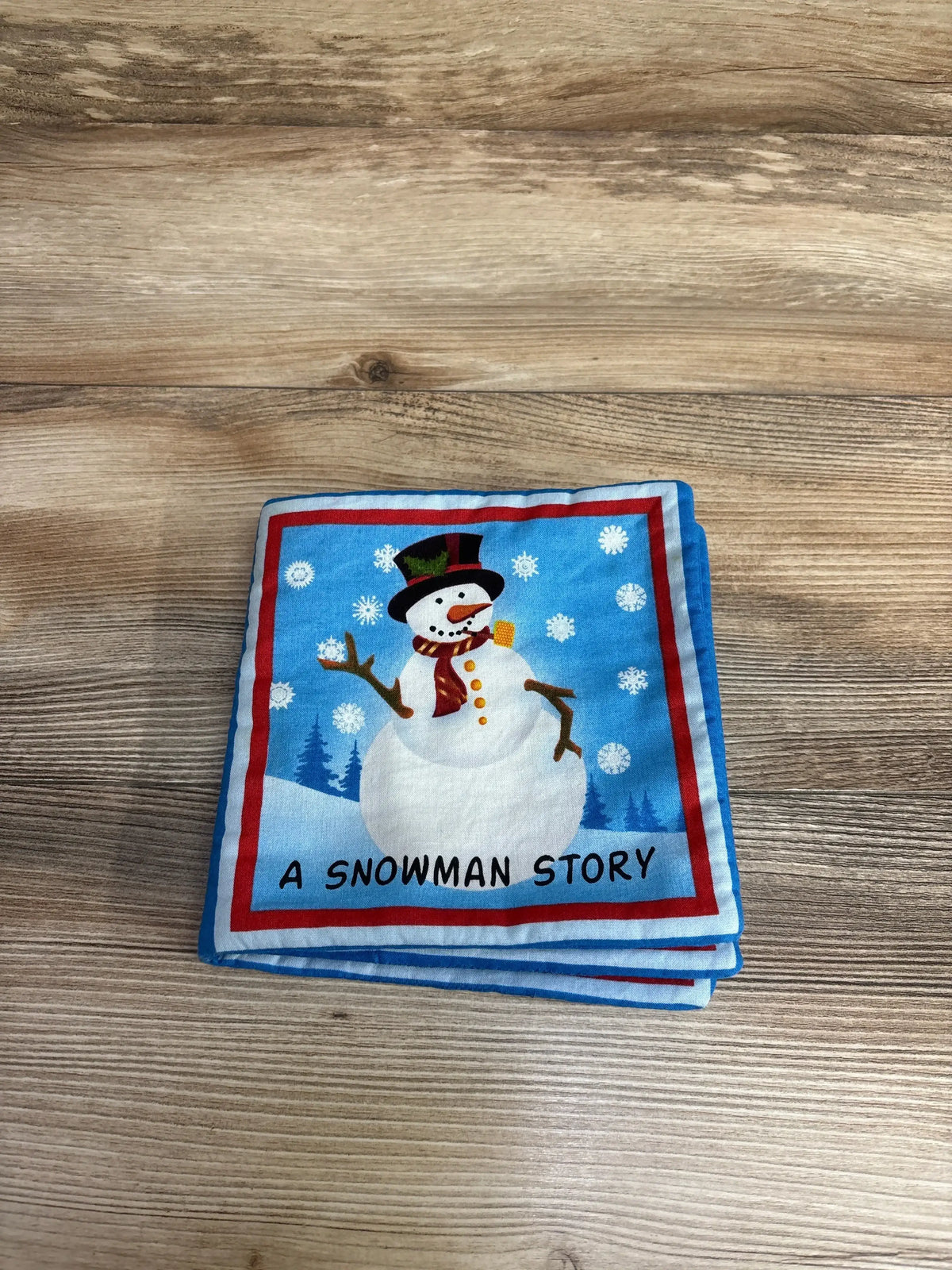 Children’s cloth book with snowman illustration on wood surface, titled A Snowman Story