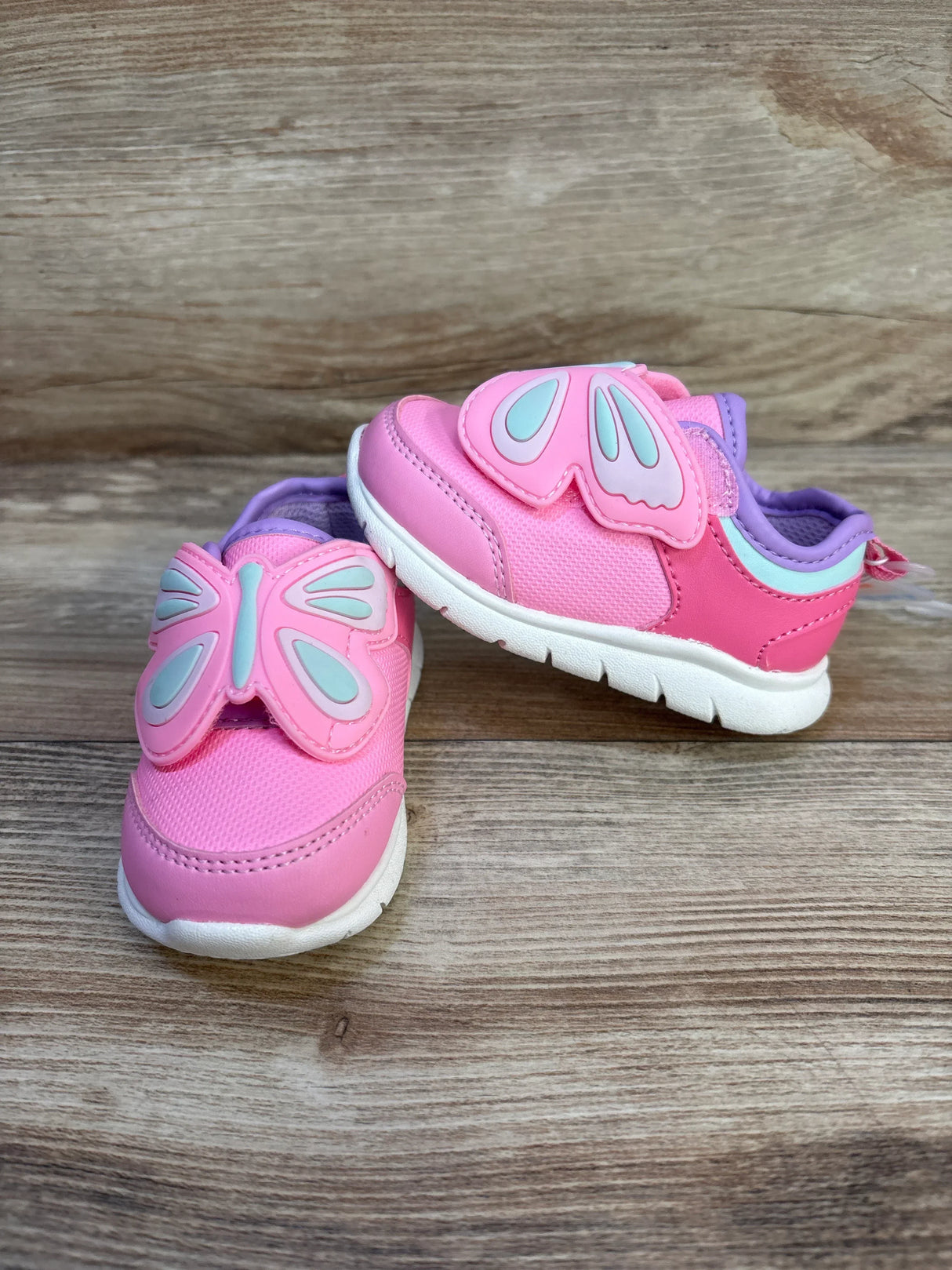 Pink toddler sneakers with butterfly wing design on wooden floor