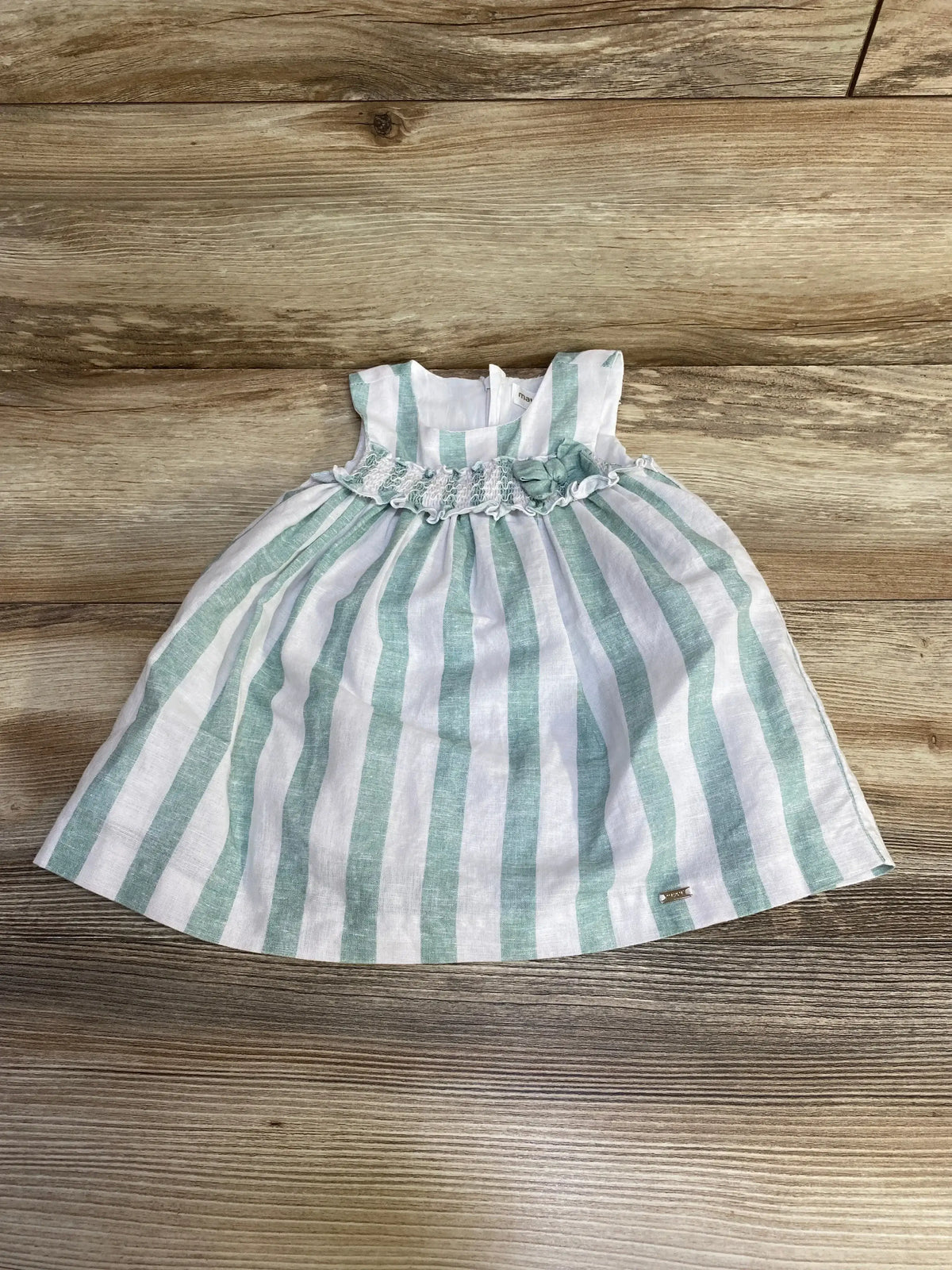 Flat lay of Mayoral green-and-white striped linen-blend baby dress showing smocked waist with rosette on wood background