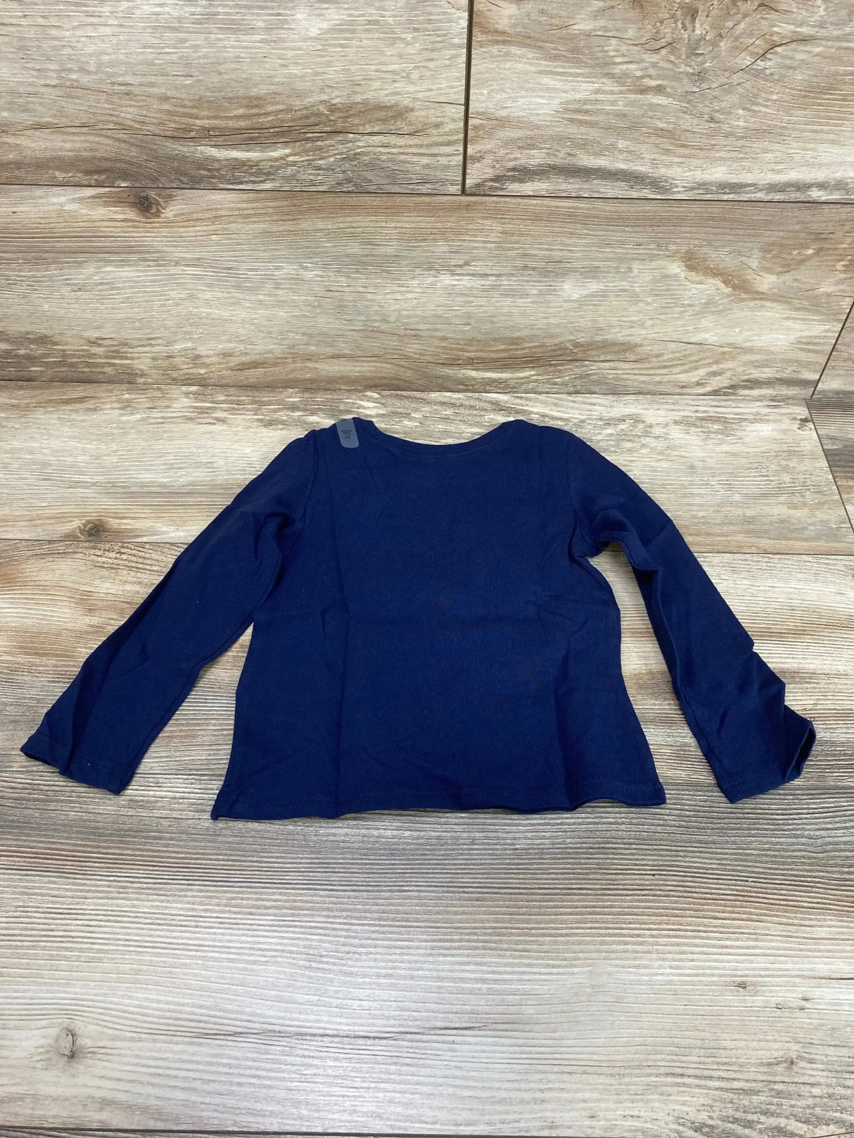 Flat lay of toddler navy long-sleeve Children's Place gymnastics shirt showing scoop neckline and shoulder size tag on wooden floor background