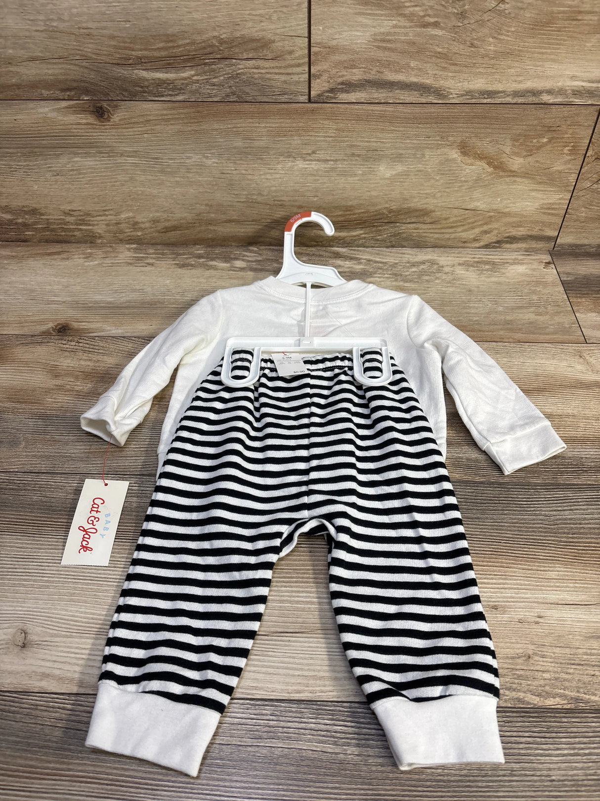 Flat-lay of Cat & Jack infant two-piece set with white long-sleeve top and black-and-white striped jogger pants on a wood floor background