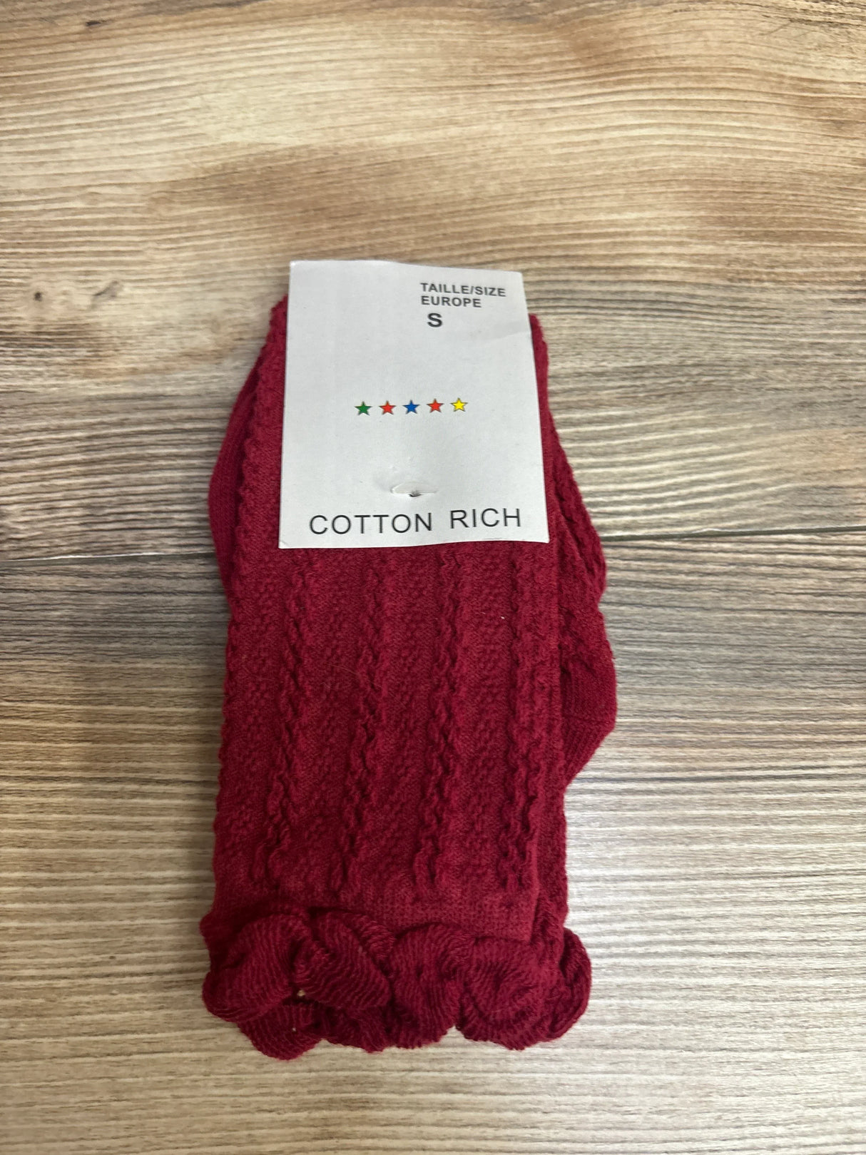 Front view of red cotton rich knitted socks showcasing cable-knit texture and ruffled cuffs on a wood background