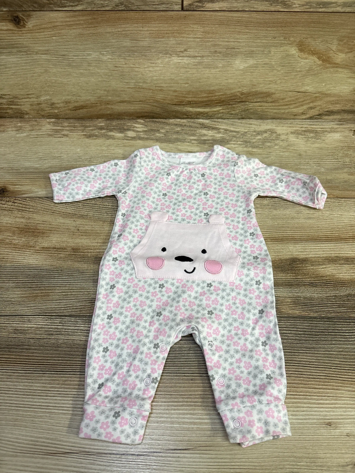 Front view of the Starting Out sleeper showcasing a pink floral pattern, bunny face pocket, and snap closures on a wood-grain background