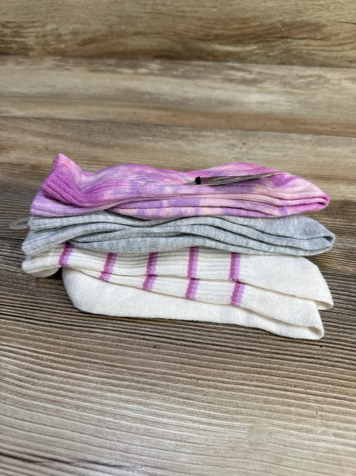 Side view of three-pack Art Class crew socks showcasing pink tie-dye, heather gray, and white with pink stripes on a wood background