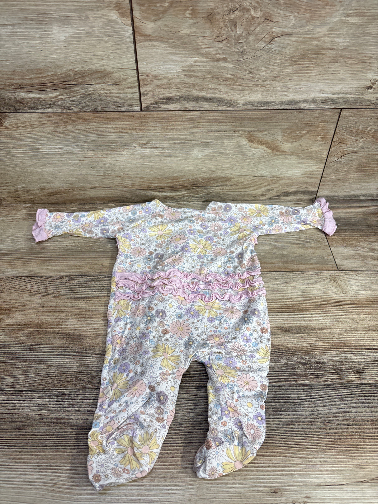 Infant floral print sleeper with pink ruffles and ruffle cuffs laid flat on wooden floor