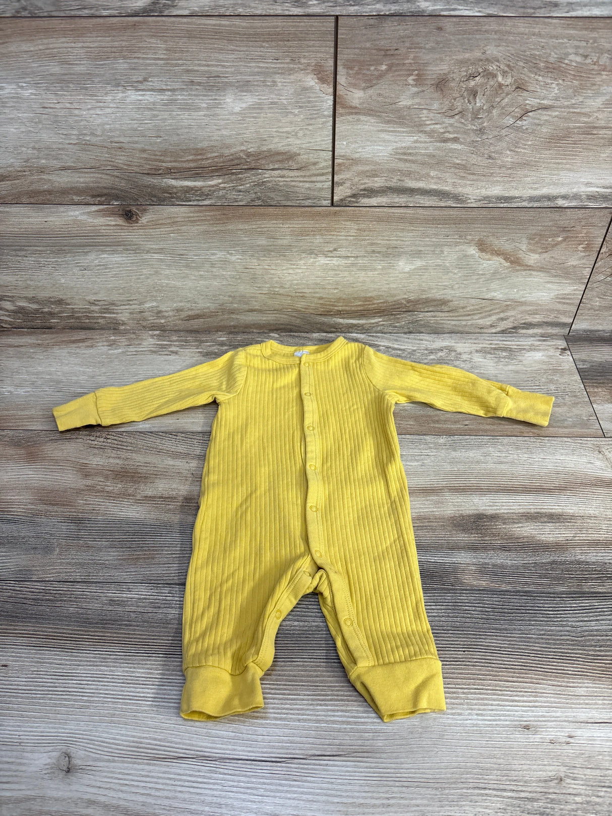 Yellow ribbed baby onesie laid flat on wooden floor